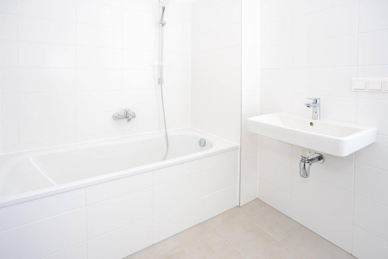 Helles Badezimmer mit Badewanne, Duscharmatur und einem modernen Waschbecken, komplett gefliest.