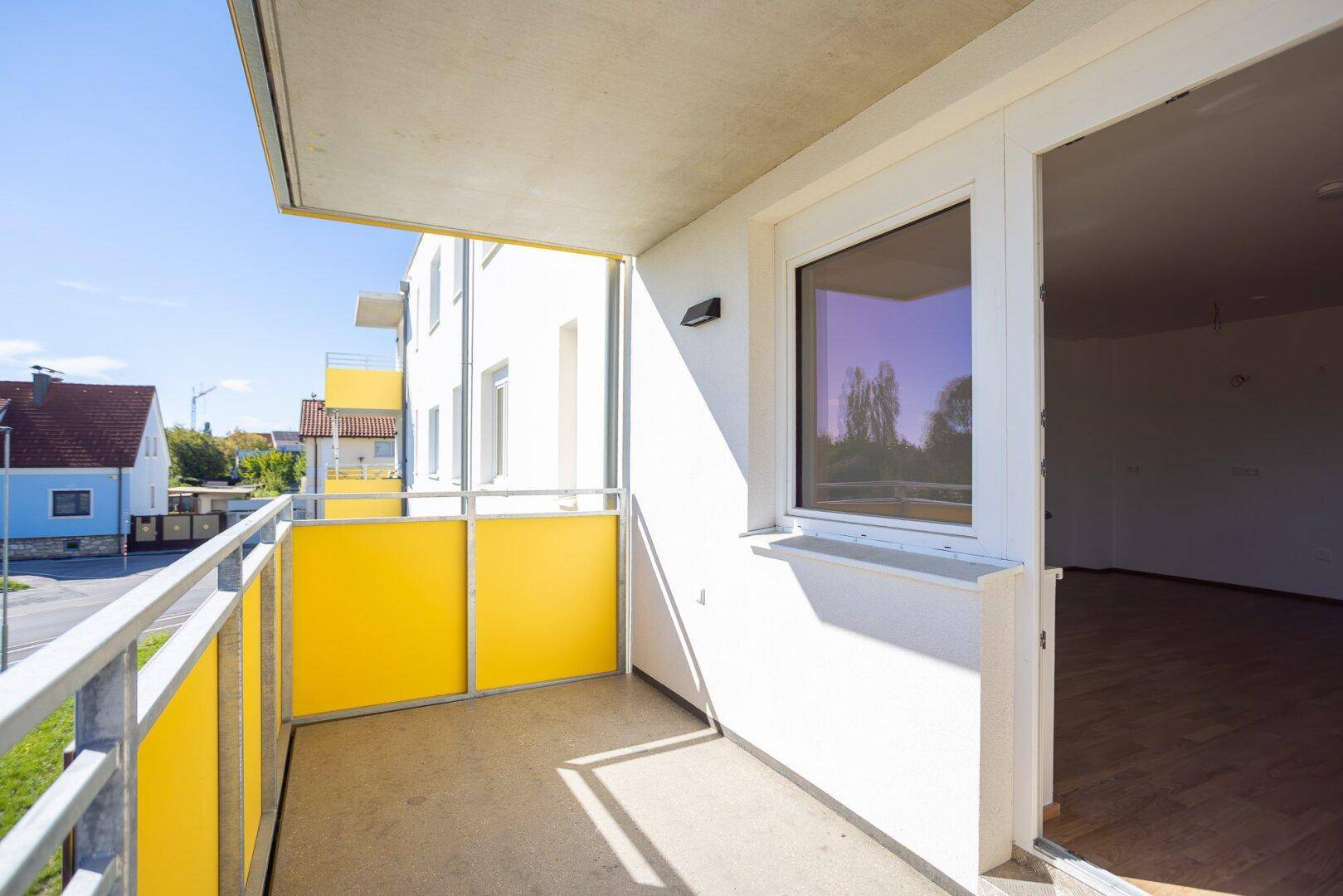 Heller Balkon mit gelben Akzenten und Blick auf die umliegenden Gebäude und die Nachbarschaft.