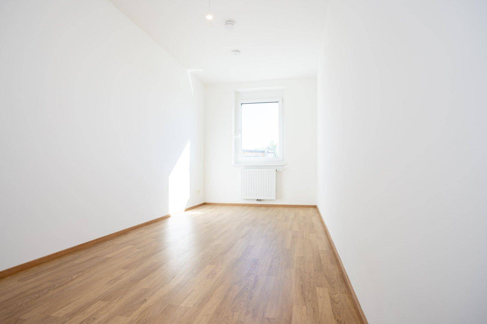 Helles Zimmer mit Laminatboden und einem Fenster, das viel Tageslicht in den Raum bringt.