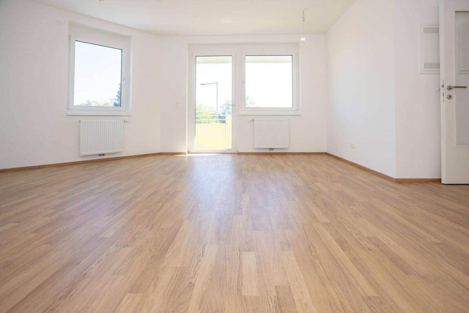 Großes, helles Zimmer mit Laminatboden und Zugang zu einem sonnigen Balkon, ideal für Wohnzwecke.
