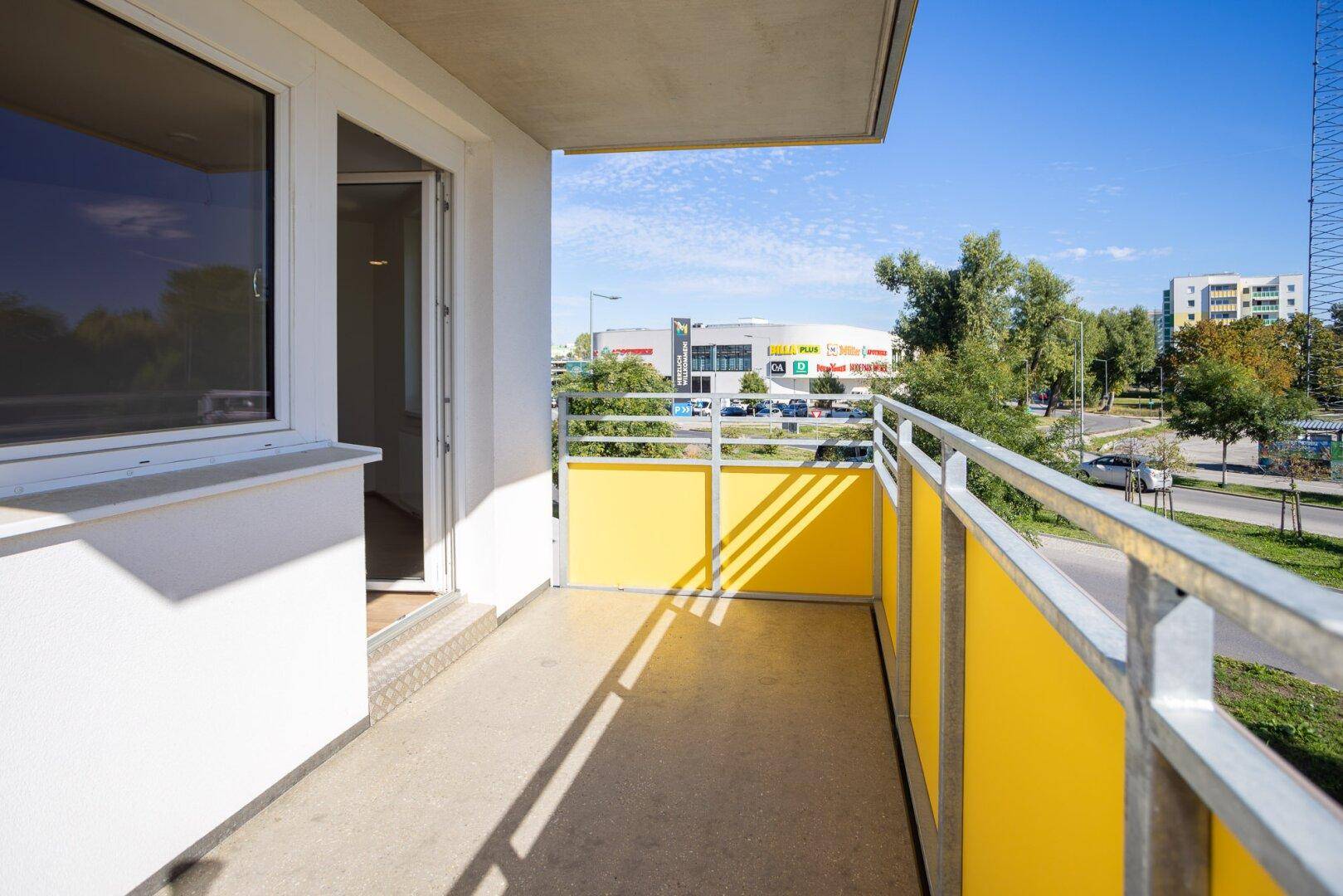 Langer Balkon mit gelben Brüstungselementen und Blick auf die Umgebung und ein Einkaufszentrum.