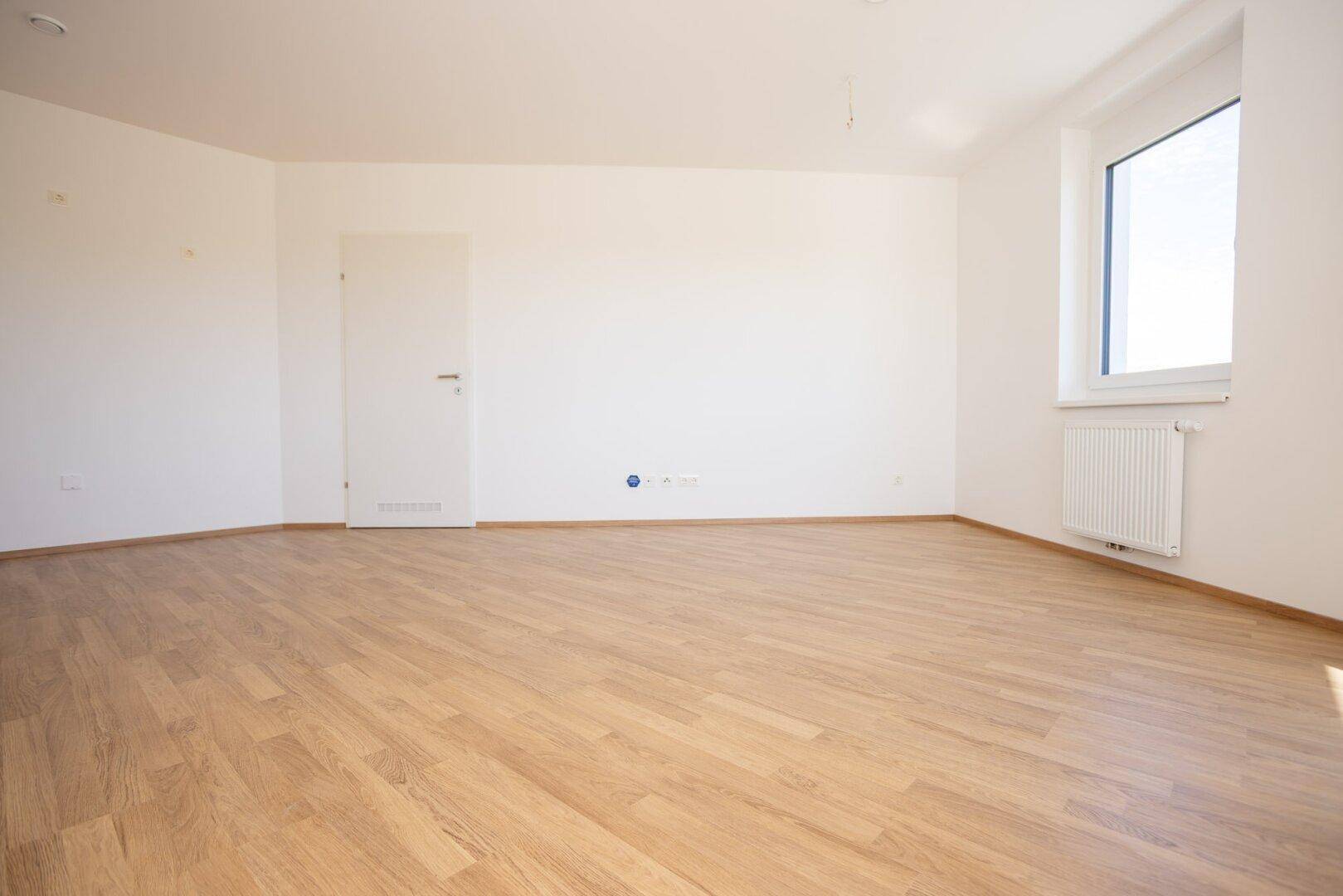 Helles Zimmer mit Laminatboden und einem großen Fenster, das viel Tageslicht hereinlässt.