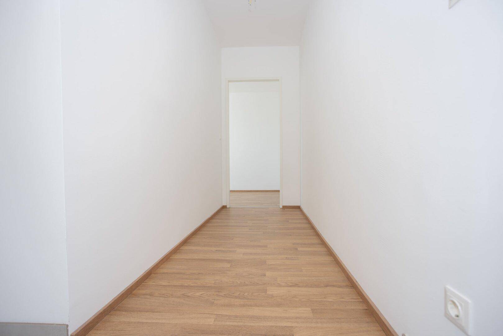 Heller Flur mit Laminatboden und weißen Wänden, der zu weiteren Räumen führt.