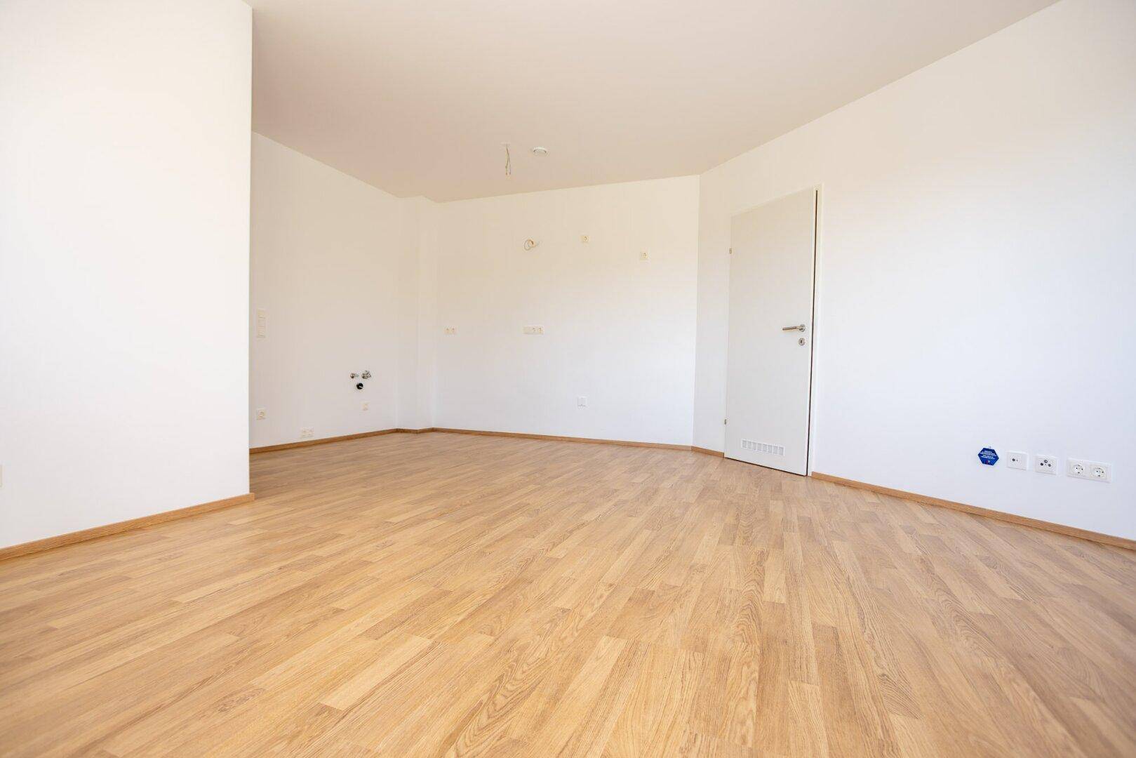 Leeres Zimmer mit hellem Laminatboden und weißen Wänden, bietet vielseitige Gestaltungsmöglichkeiten.