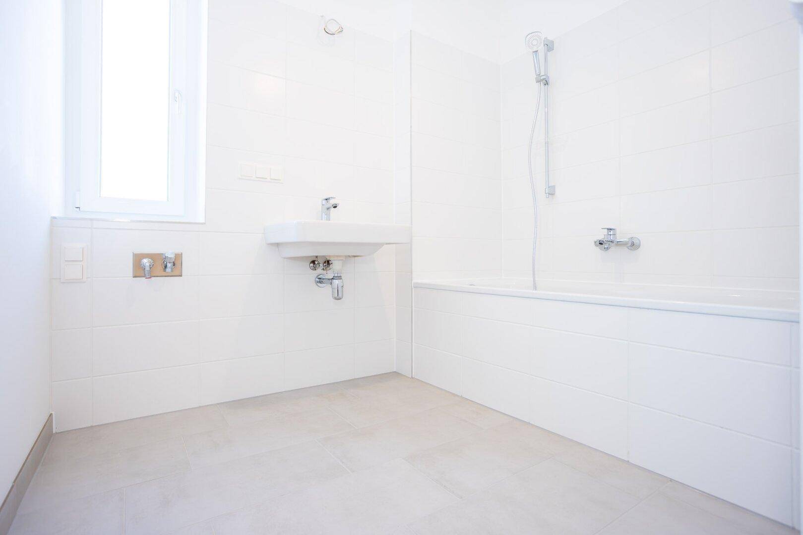 Modernes Badezimmer mit weißen Fliesen, Badewanne und Fenster für natürliches Licht.