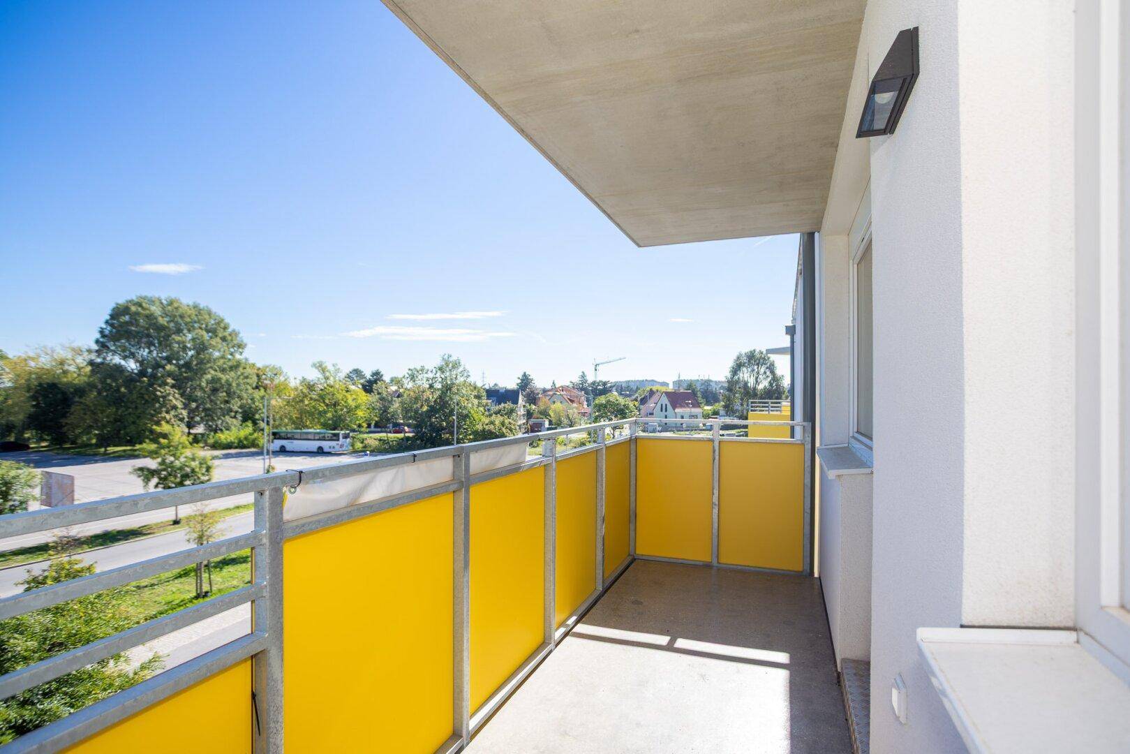 Heller Balkon mit gelben Sichtschutzelementen und Blick auf die grüne Umgebung.
