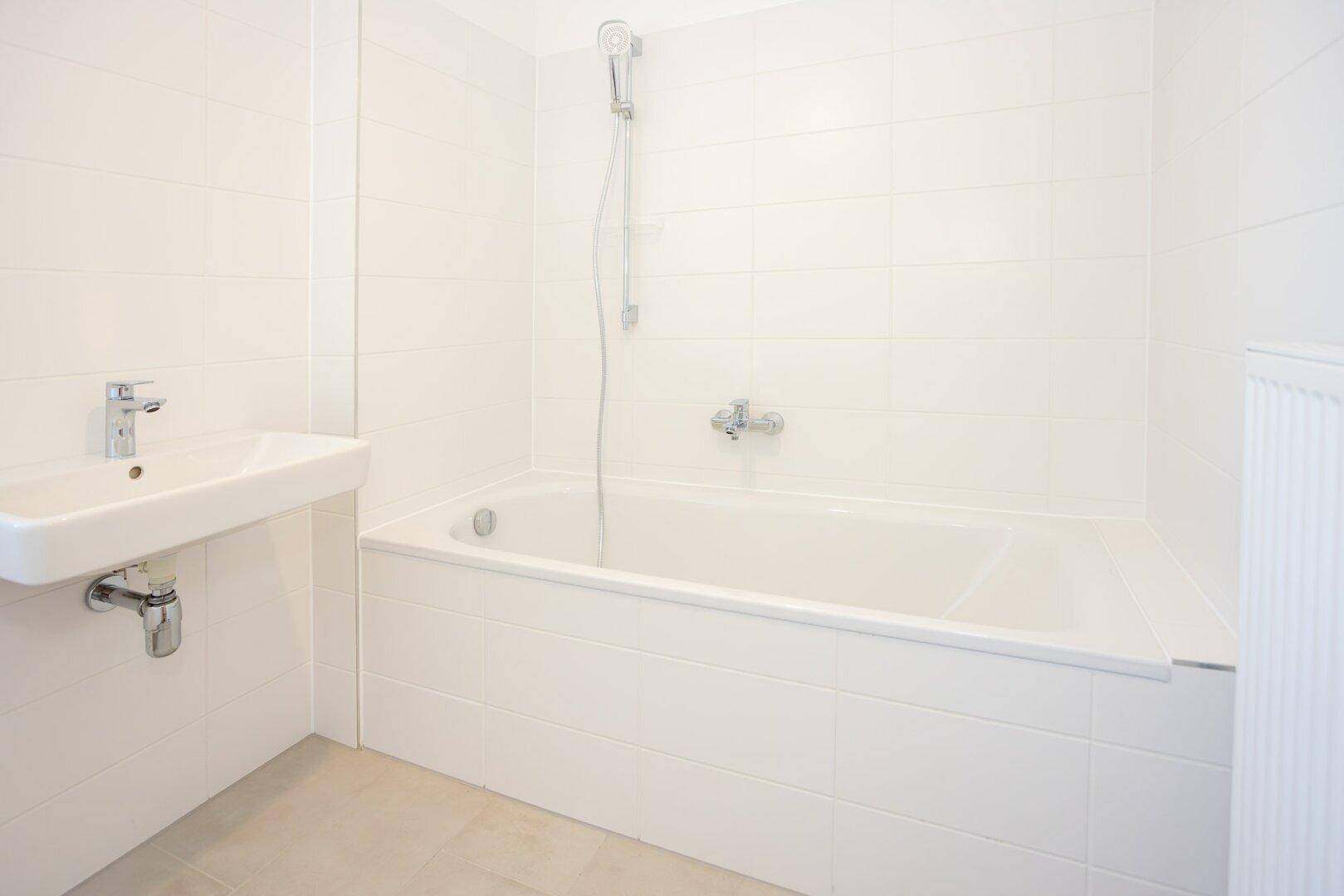 Helles Badezimmer mit weiß gefliesten Wänden, Badewanne und modernem Waschbecken.