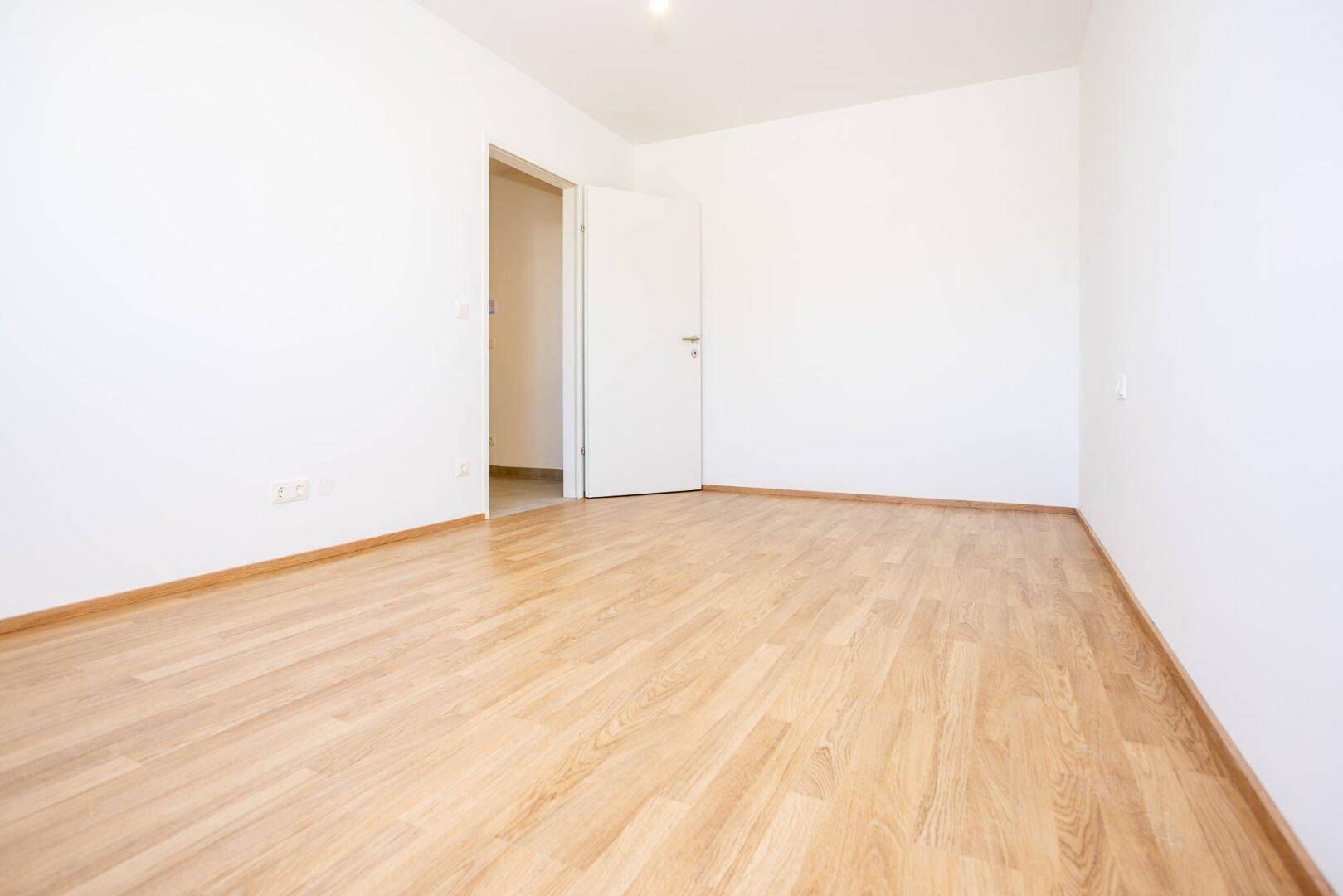 Geräumiges, helles Zimmer mit Laminatboden und Zugang zu weiteren Räumen der Wohnung.
