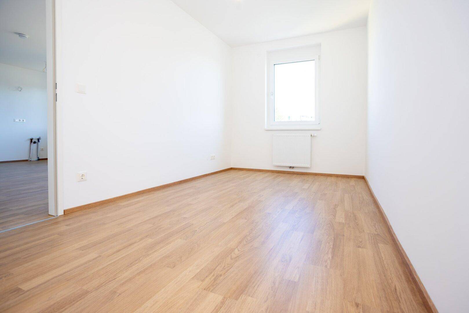 Ruhiges Zimmer mit Laminatboden und einem Fenster, das eine angenehme Atmosphäre schafft.