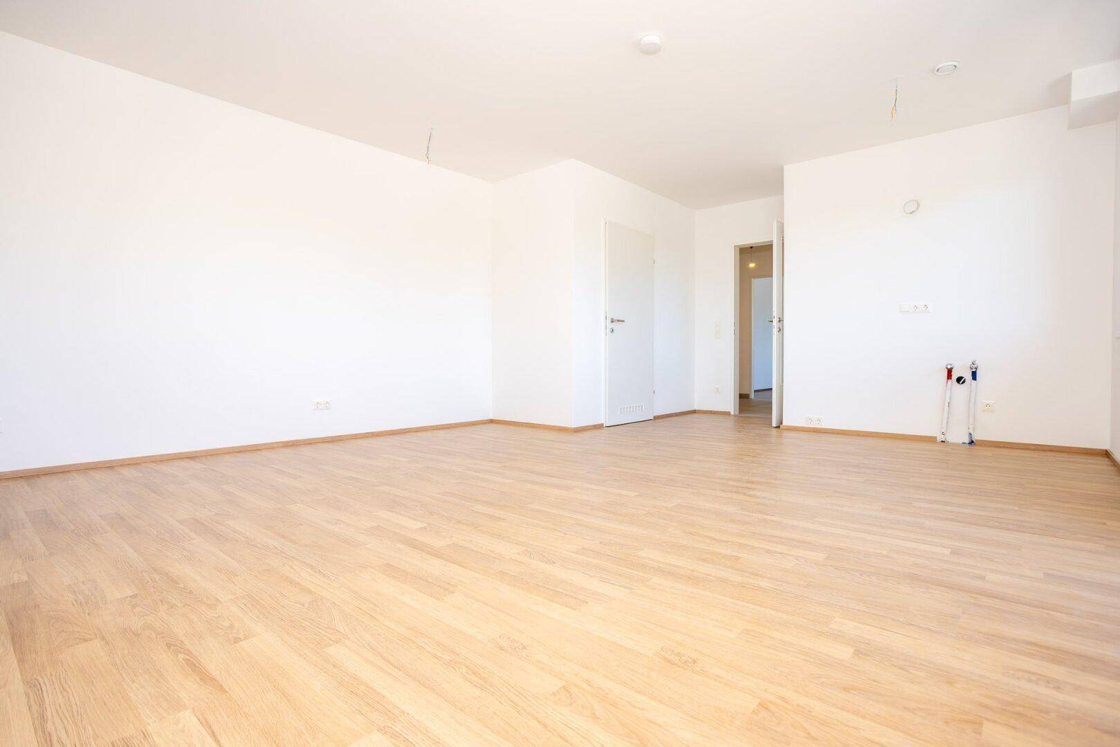 Leerer Raum mit Laminatboden und vorbereiteten Anschlüssen, ideal für eine Küche oder Hauswirtschaftsraum.