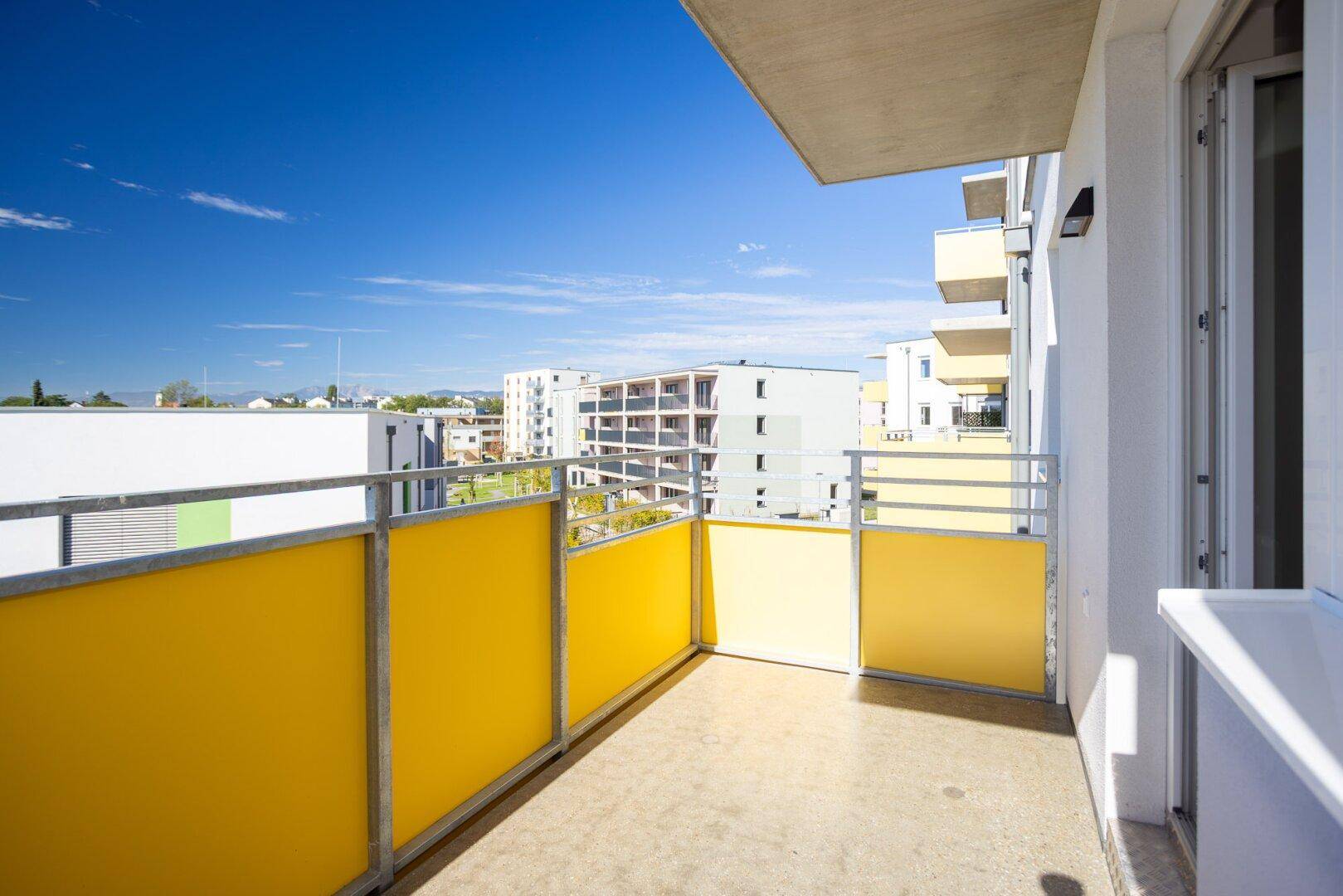 Heller Balkon mit gelben Brüstungselementen und weitem Blick über die Nachbarschaft.