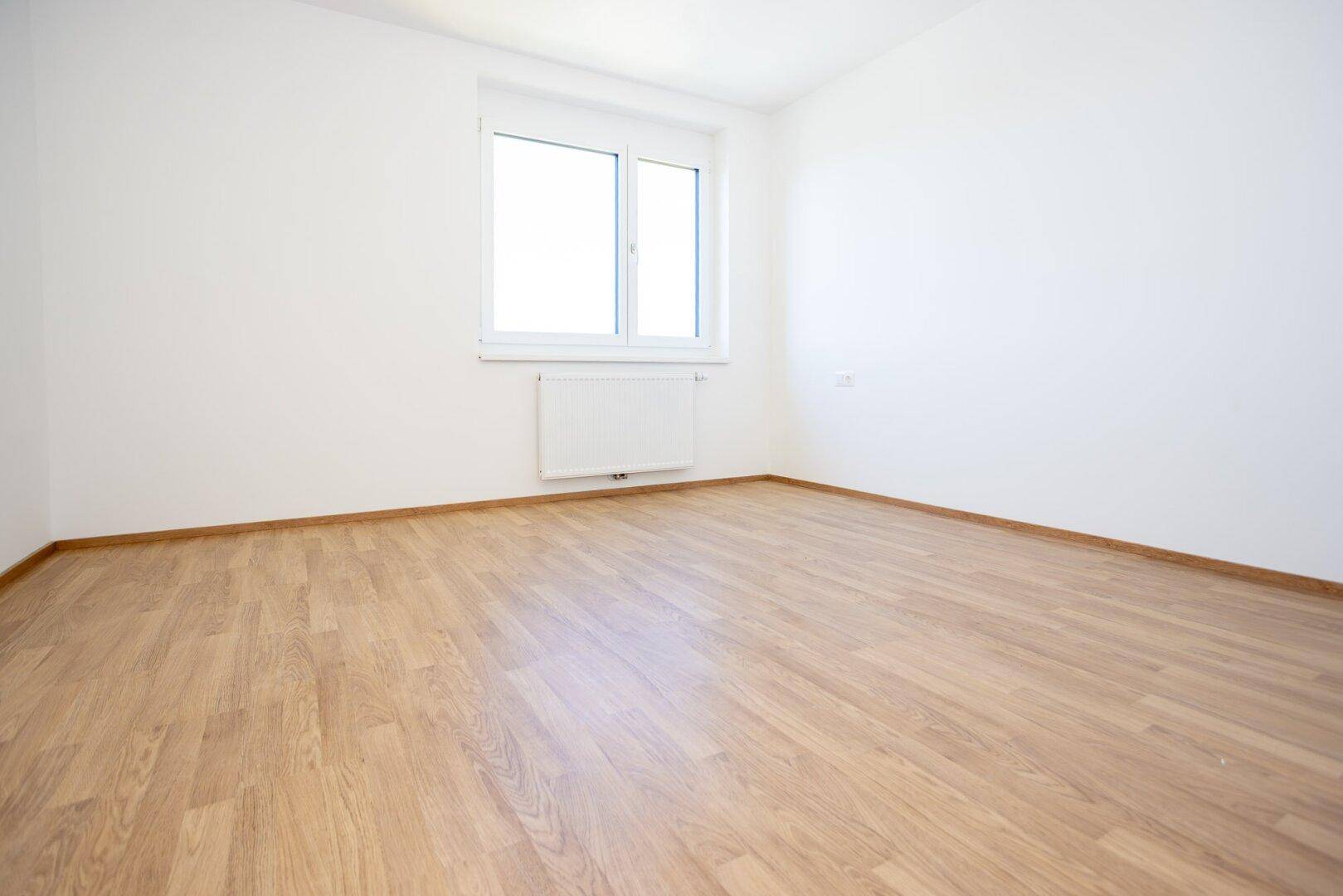 Helles, unmöbliertes Schlafzimmer mit Laminatboden und großem Fenster.