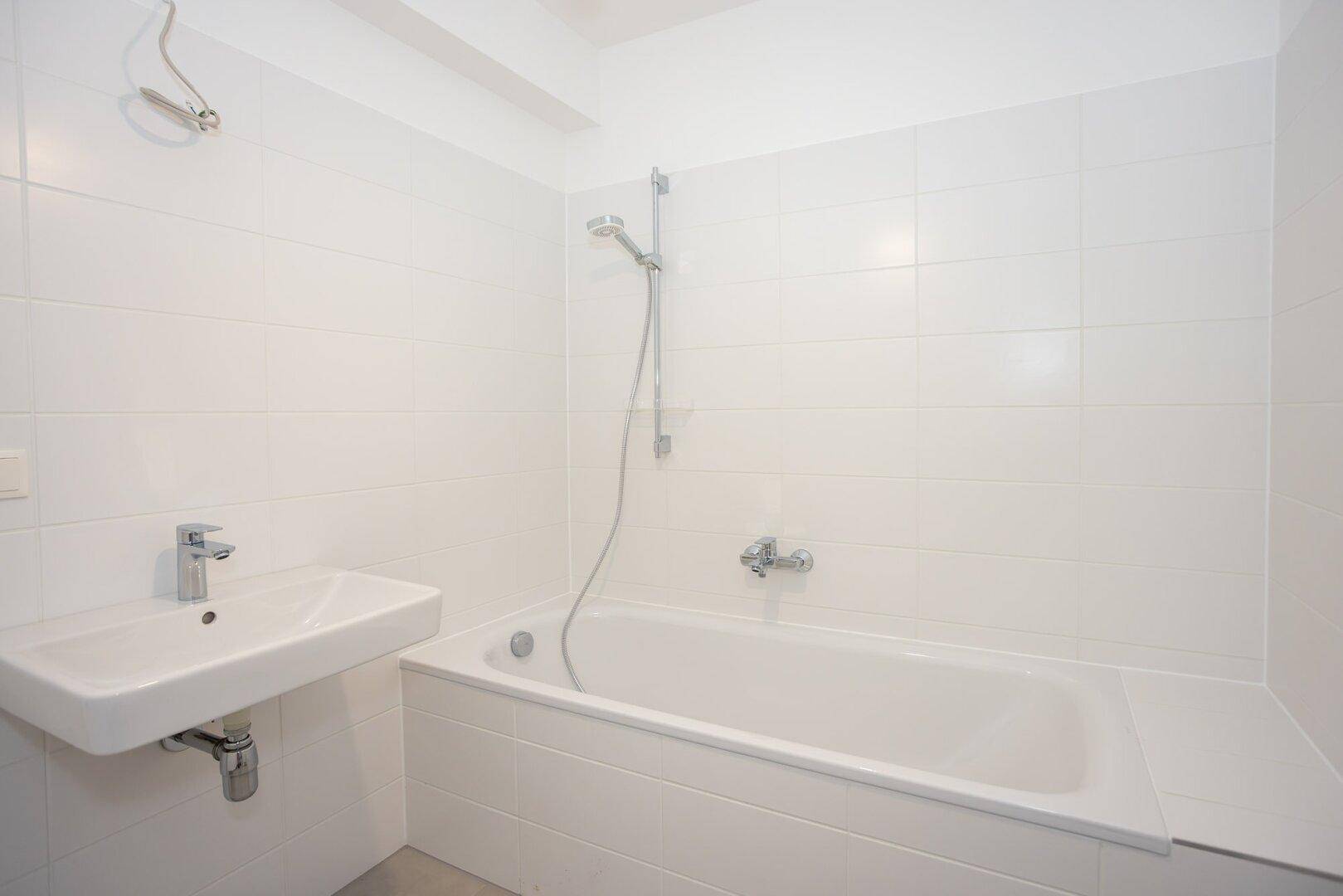 Helles Badezimmer mit Badewanne, Waschbecken und weißen Wandfliesen.