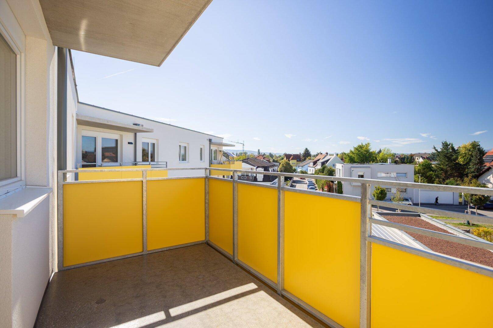 Sonniger Balkon mit gelben Sichtschutzelementen und Blick auf die Umgebung.