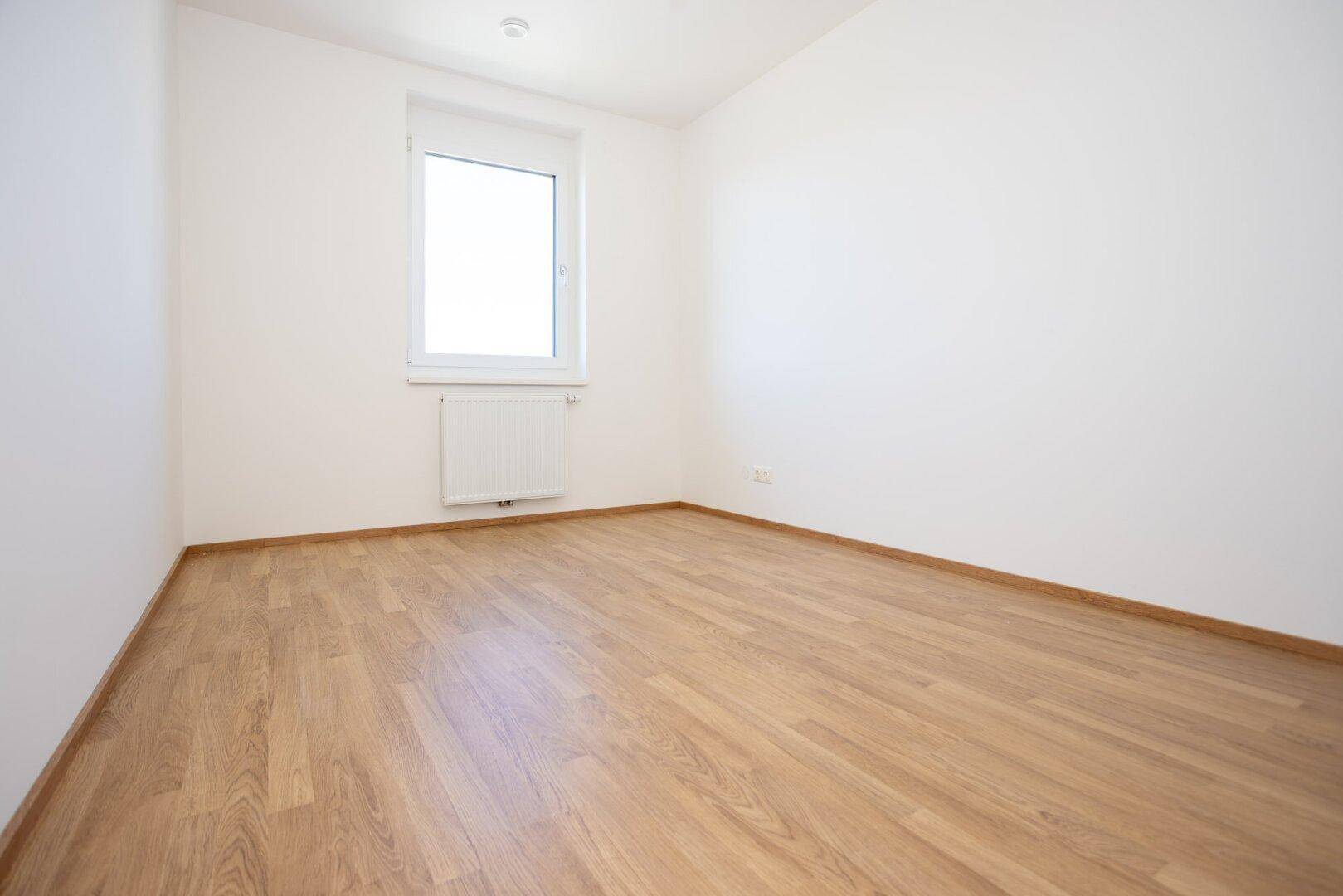 Leeres Schlafzimmer mit Laminatboden, weiß gestrichenen Wänden und Fenster.
