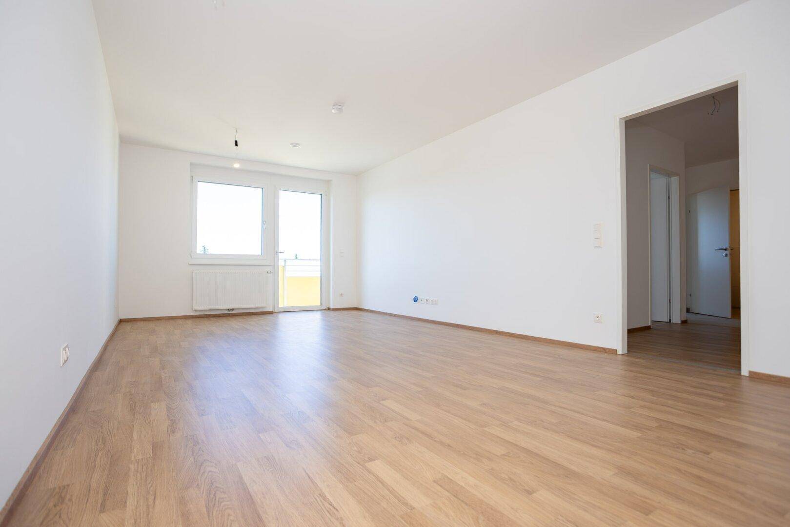 Geräumiges, unmöbliertes Wohnzimmer mit Laminatboden und hellem Tageslicht.