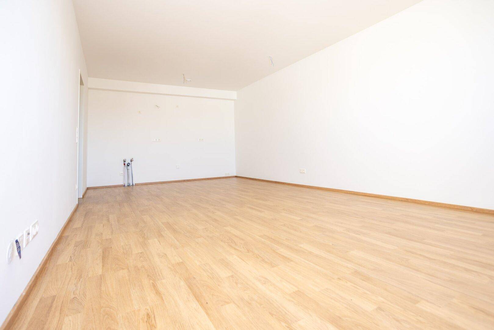 Leerer Küchenbereich mit Anschlüssen für Geräte und Laminatboden.