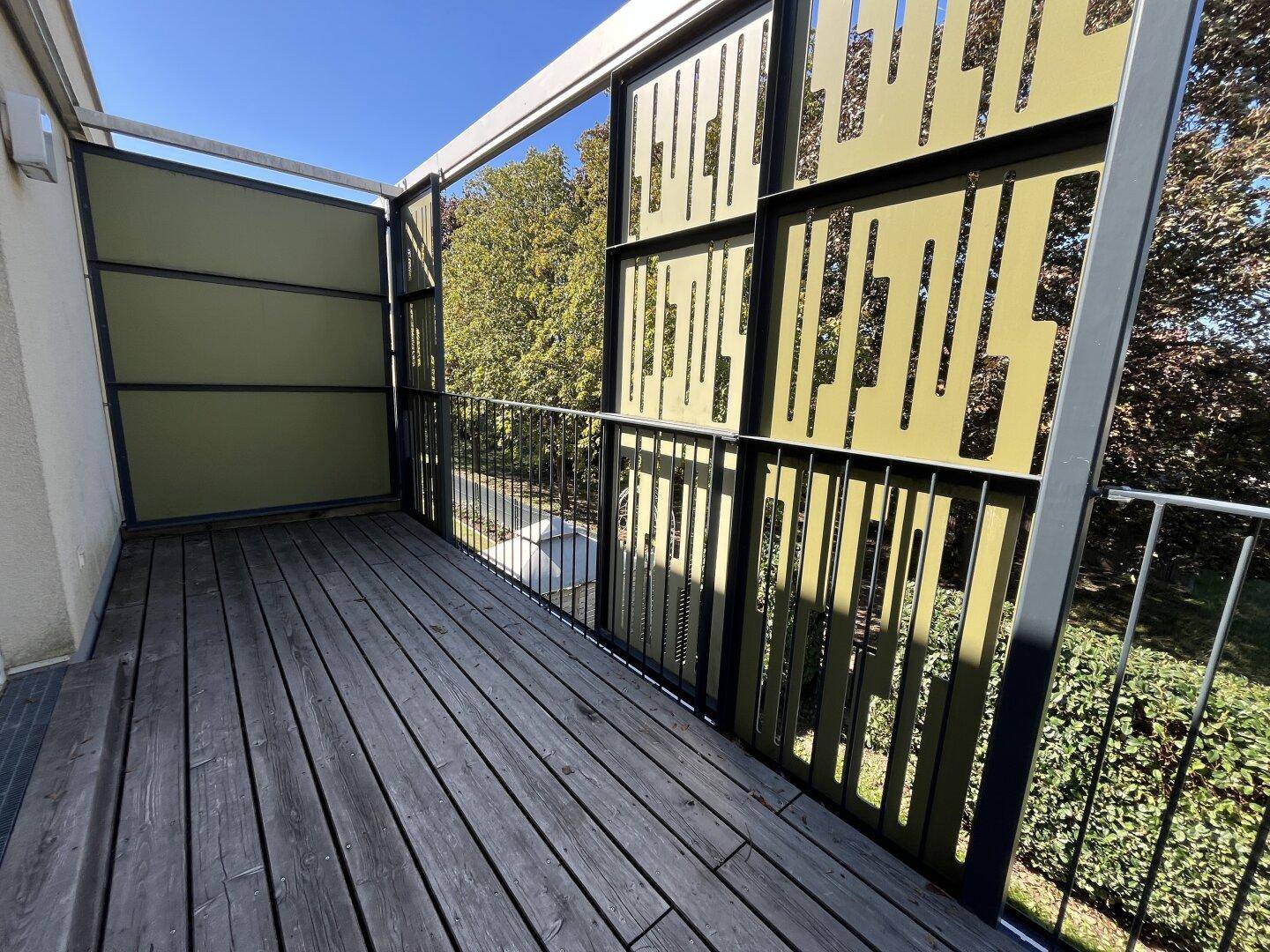 Geräumiger Balkon mit Holzdielen und grünen, perforierten Paneelen für Privatsphäre und Design.