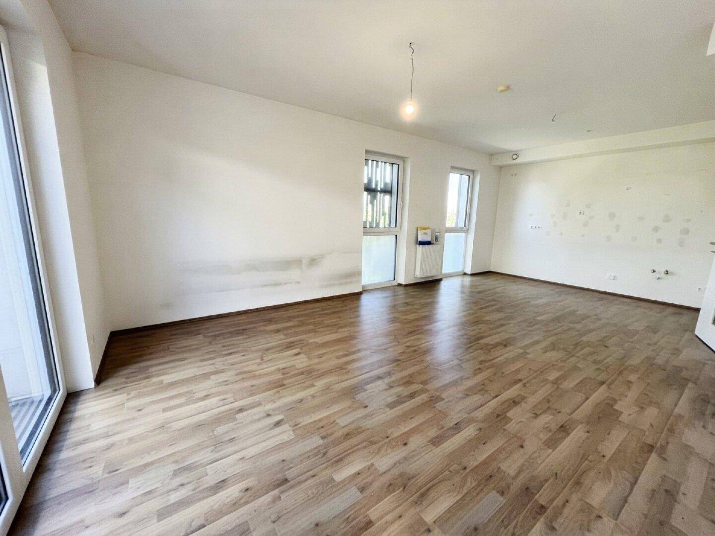 Geräumiges, unmöbliertes Wohnzimmer mit Laminatboden und großen Fenstern, bereit zur individuellen Gestaltung.
