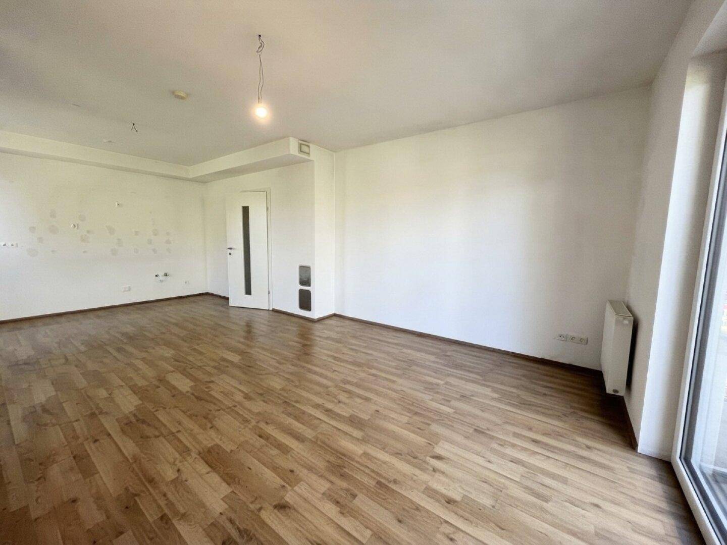 Leeres Wohnzimmer mit Laminatboden und weiß gestrichenen Wänden, bietet viel Raum für Gestaltungsideen.