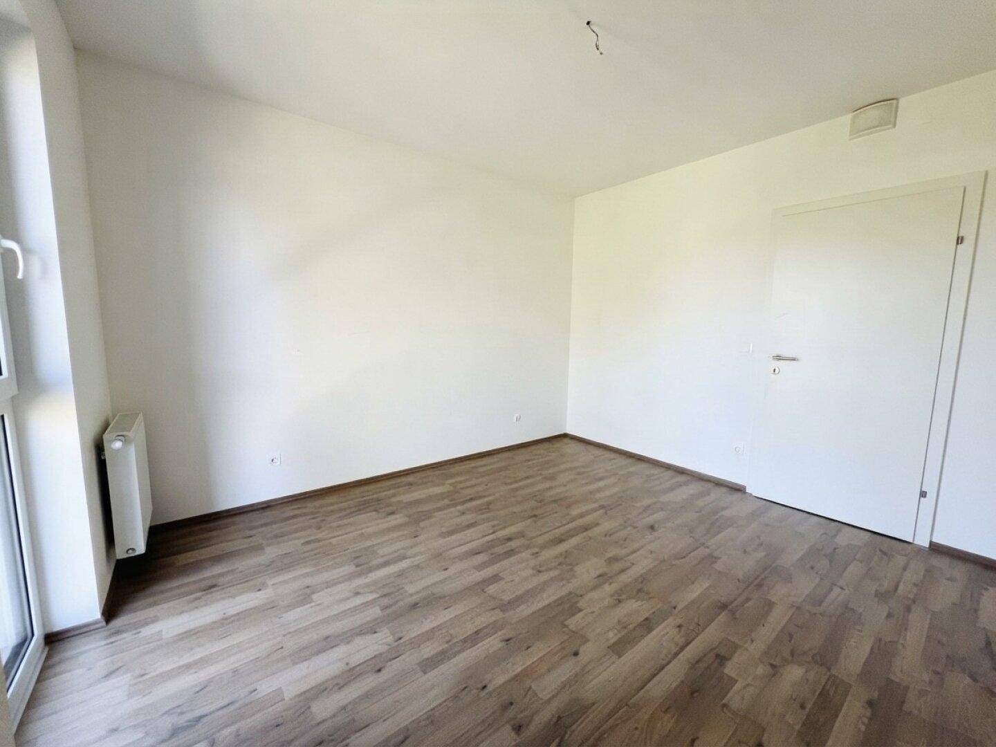 Unmöbliertes Schlafzimmer mit Laminatboden und einem Fenster, das einen Blick ins Grüne bietet.