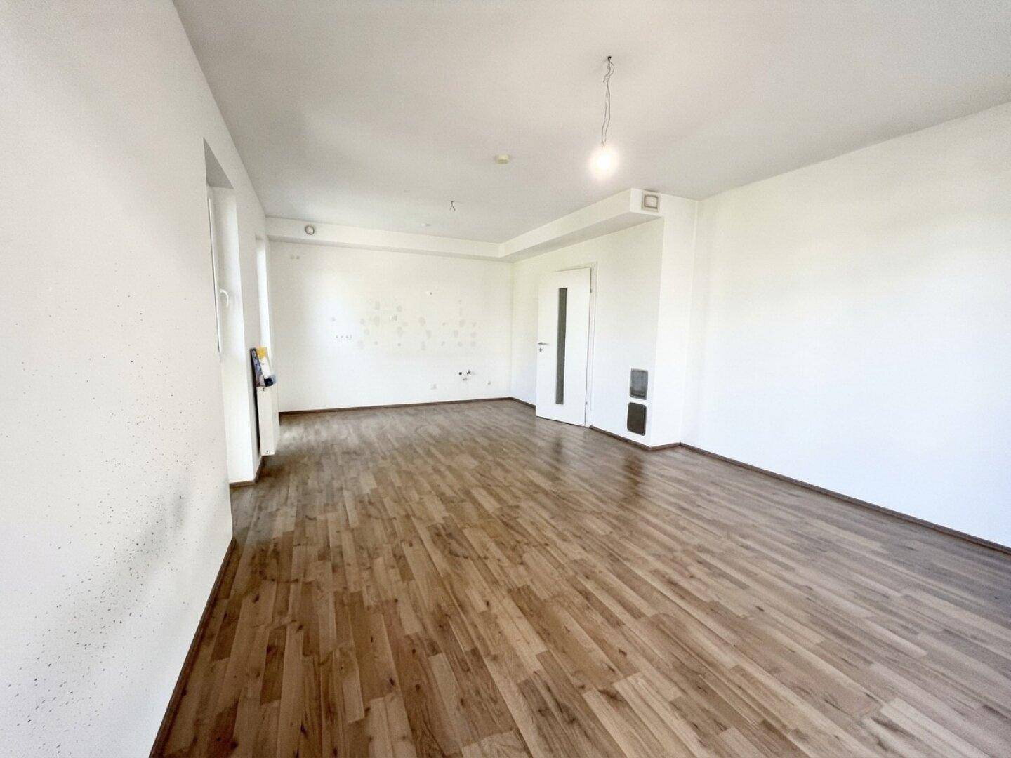 Heller, unmöblierter Raum mit Laminatboden und schlichten weißen Wänden, ideal für ein Wohnzimmer.