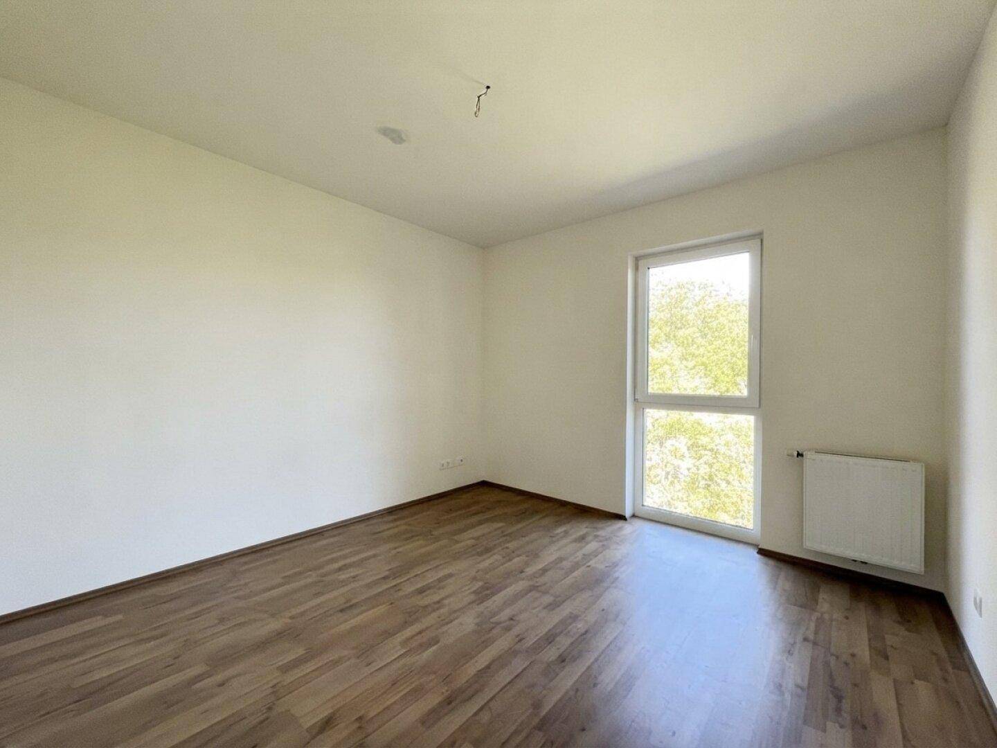 Ruhiges Schlafzimmer mit Laminatboden und einem großen Fenster, ideal für erholsame Nächte.