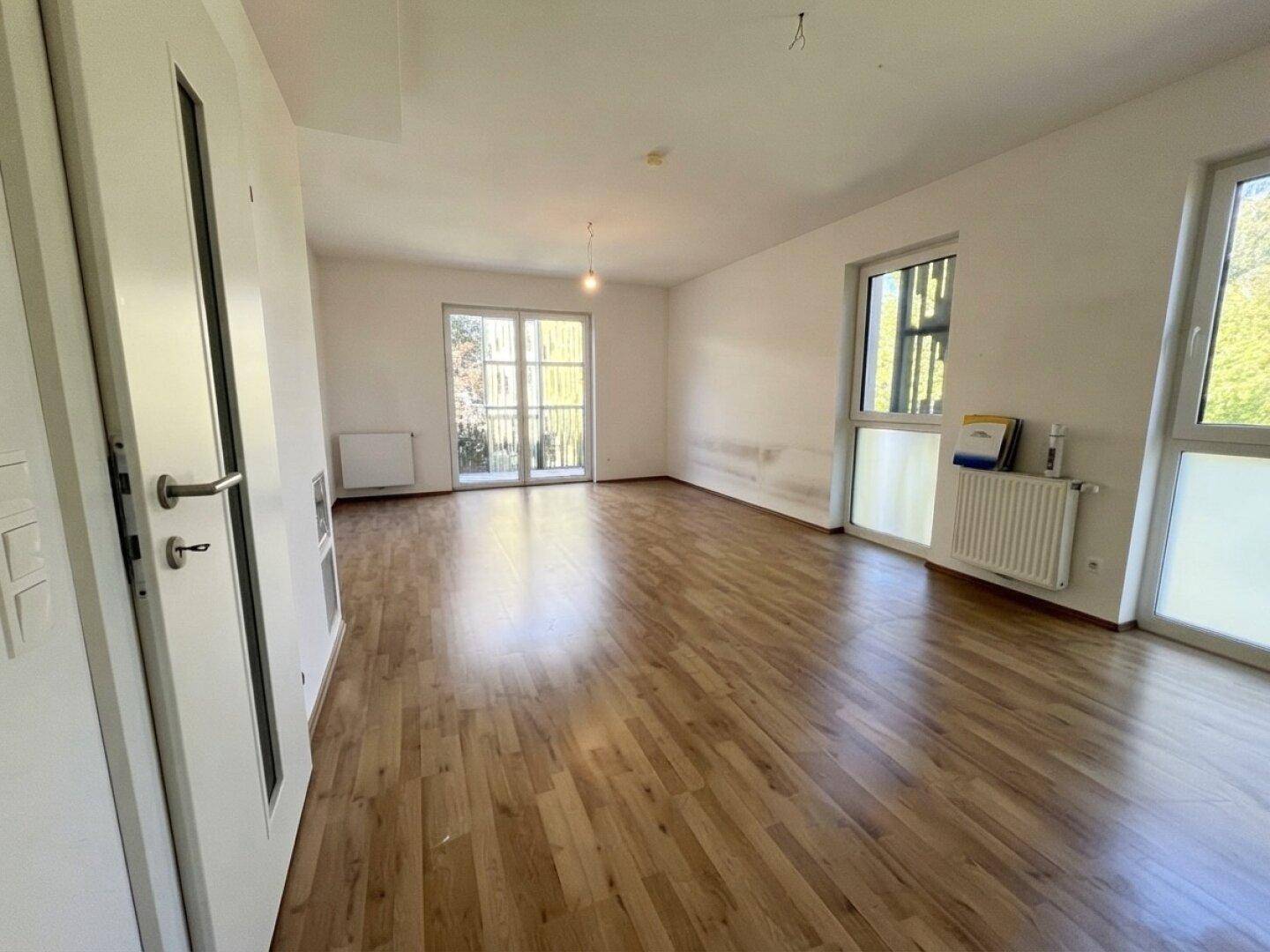 Helles, leeres Wohnzimmer mit Laminatboden und Zugang zu einem Balkon oder einer Terrasse.