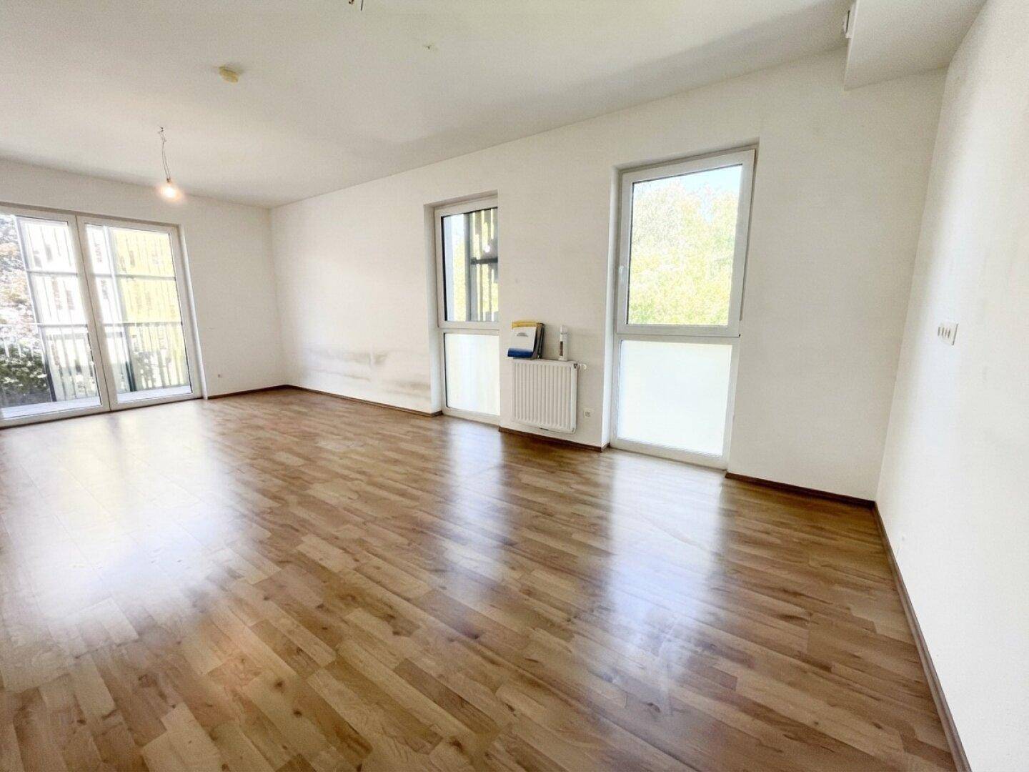 Lichtdurchflutetes Wohnzimmer mit hellem Laminatboden und mehreren Fenstern für viel Tageslicht.