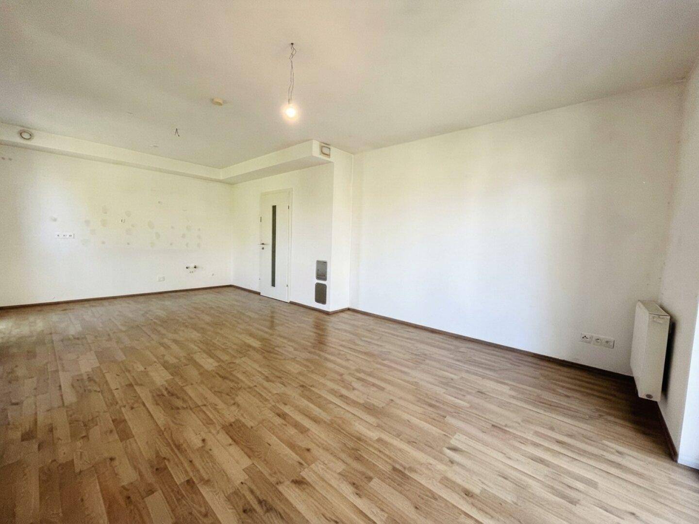 Geräumiges Wohnzimmer mit Laminatboden und neutralen Wänden, bereit für neue Bewohner.