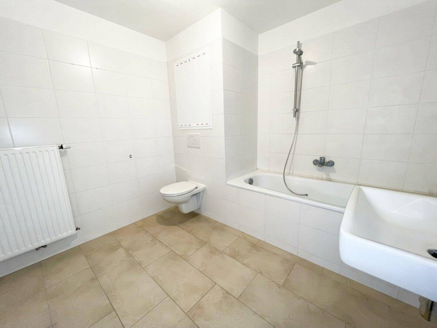 Funktionales Badezimmer mit weißen Wandfliesen, beigefarbenem Boden und Badewanne mit Duschfunktion.
