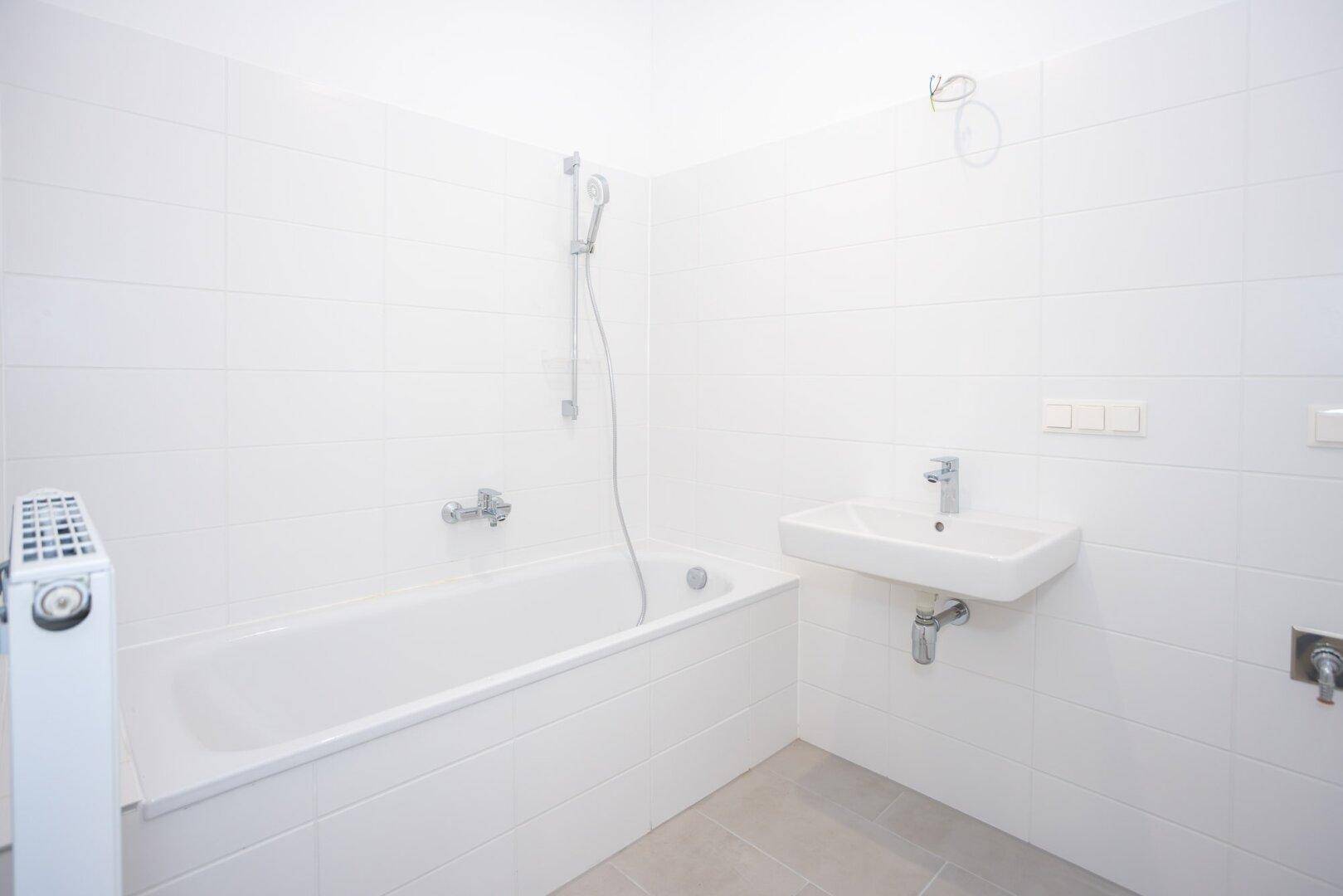 Modernes Badezimmer mit weißen Fliesen, Badewanne und Waschbecken, in neuwertigem Zustand.
