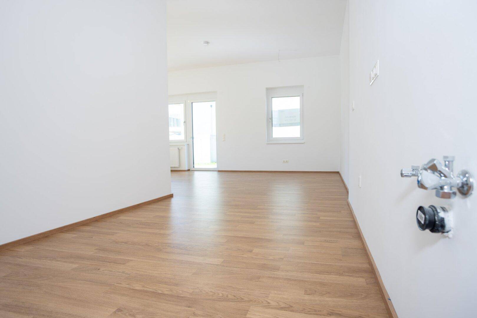 Heller Raum mit Laminatboden und Anschlüssen für eine Küche, bereit für die Installation.