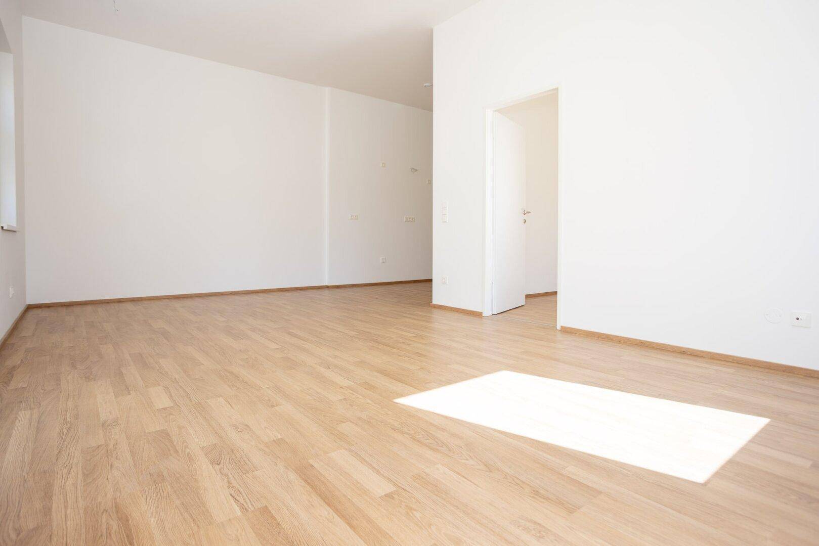 Heller Wohnraum mit Laminatboden und weiß gestrichenen Wänden, bietet viel Gestaltungspotenzial.