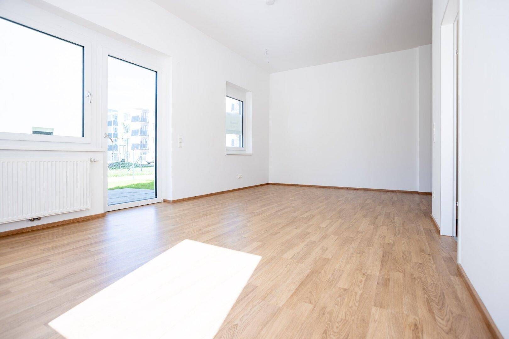 Lichtdurchflutetes Wohnzimmer mit hellem Laminatboden und weiß gestrichenen Wänden, bereit zum Einzug.