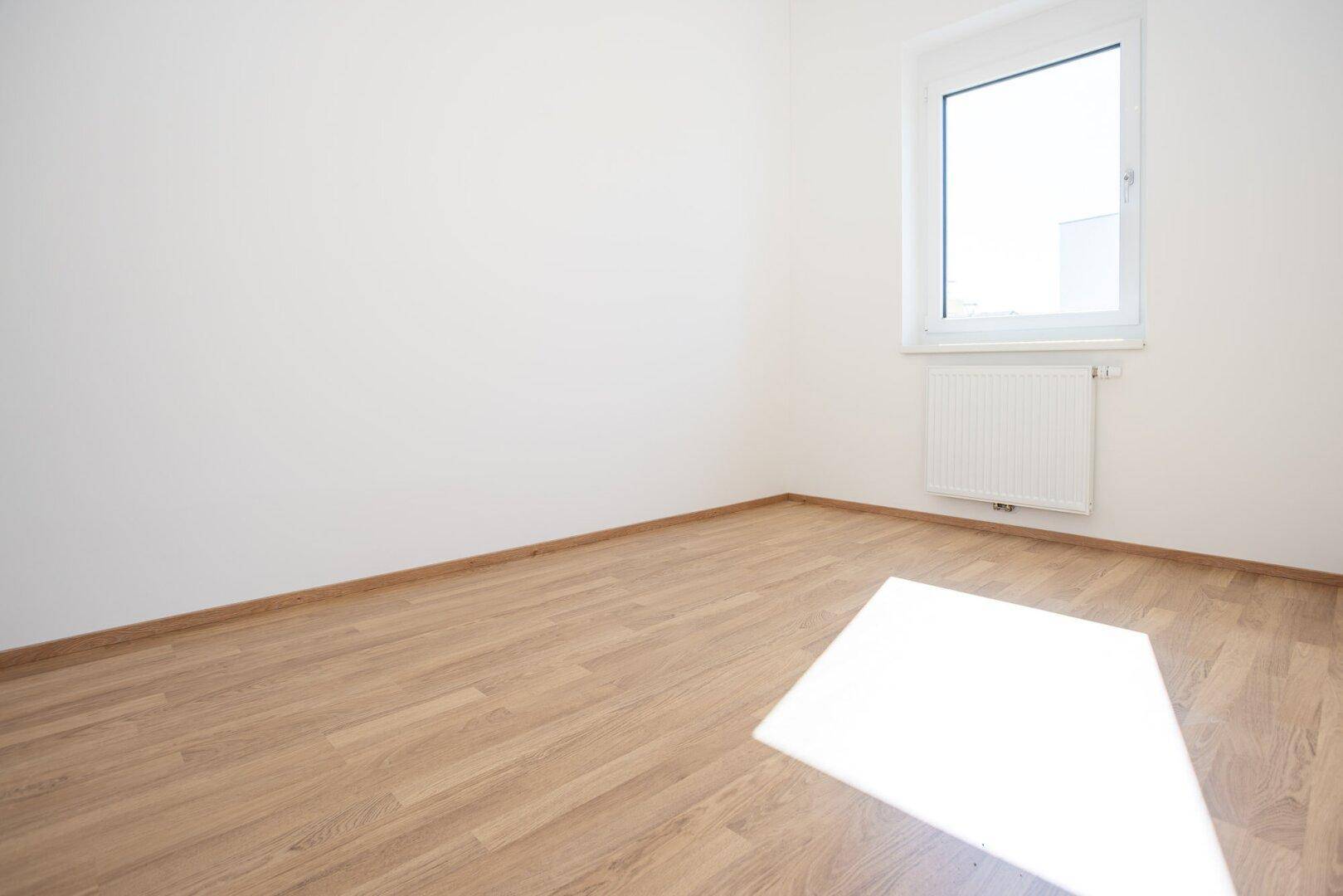 Ruhiges Schlafzimmer mit Laminatboden und Fenster, das viel Tageslicht hereinlässt.