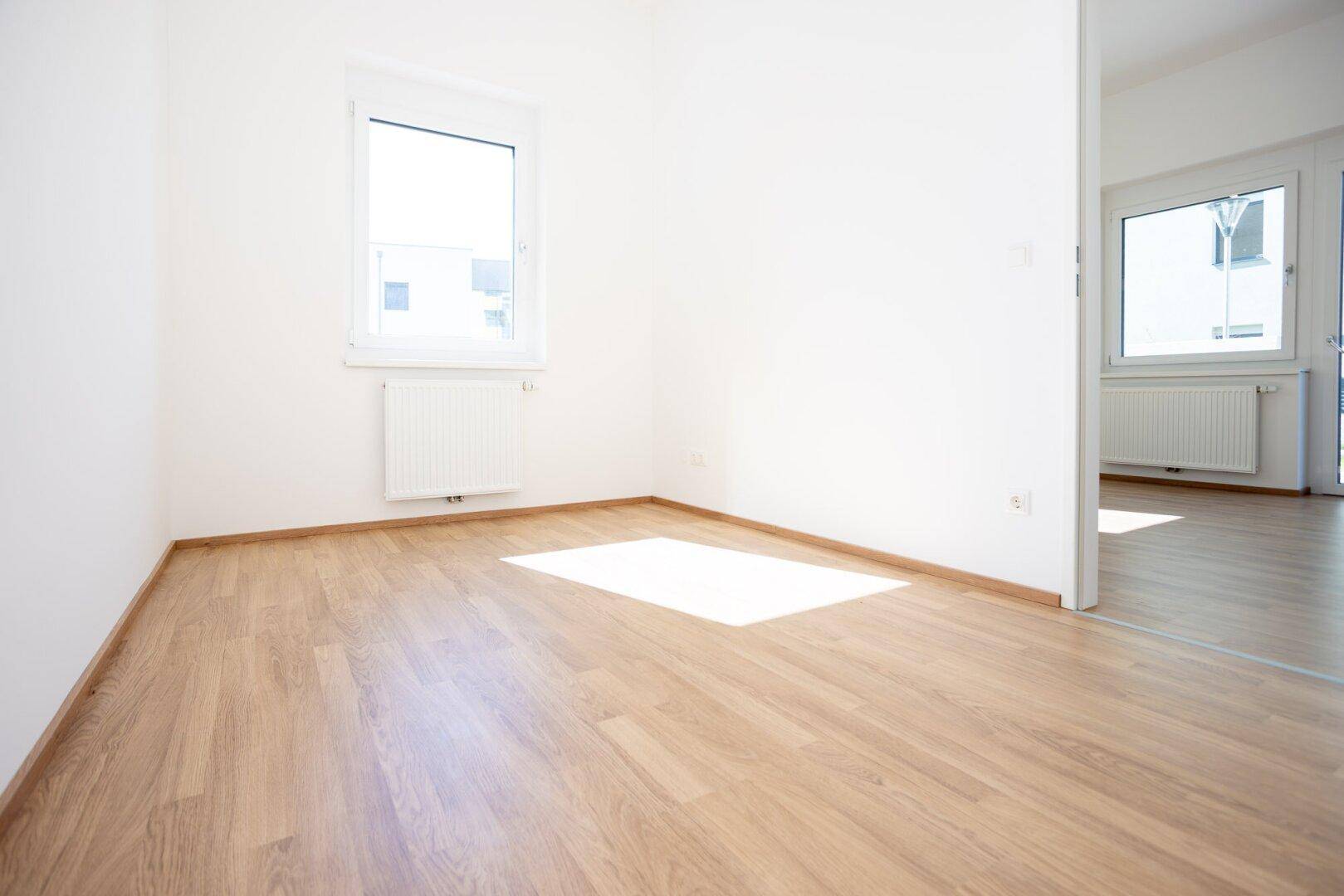 Heller Raum mit Laminatboden und Blick in einen angrenzenden Wohnbereich, ideal als Schlafzimmer.