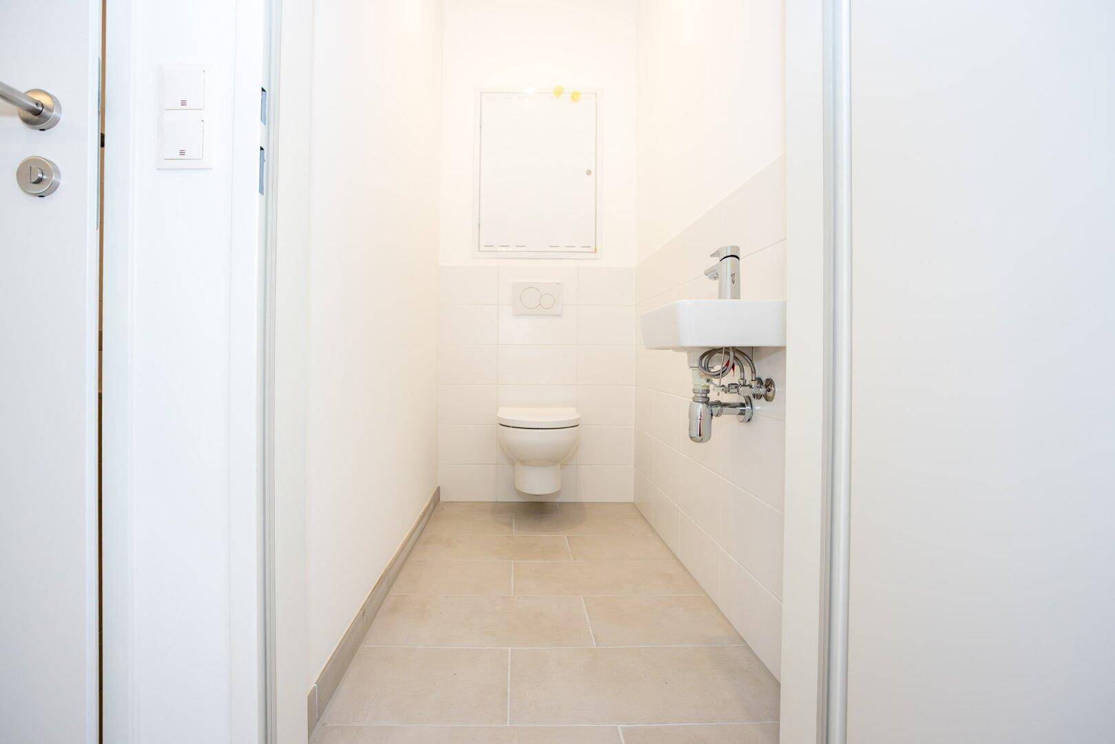 Kleines, helles Gäste-WC mit wandhängendem WC und Handwaschbecken, modern gefliest.