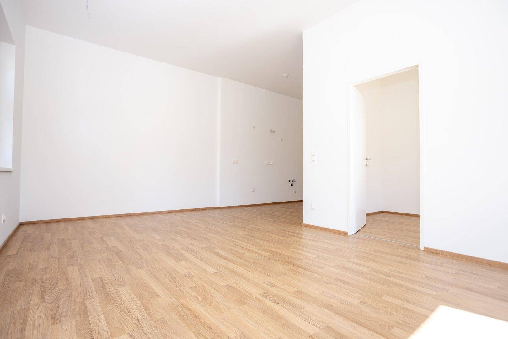 Großzügiger, leerer Wohnbereich mit Laminatboden und weißer Wandfarbe, ideal für individuelle Einrichtung.