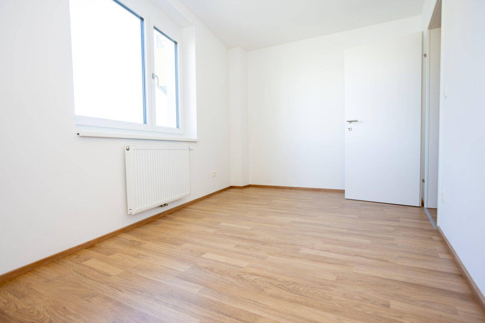 Helles Schlafzimmer mit Laminatboden, Fenster und Heizkörper.
