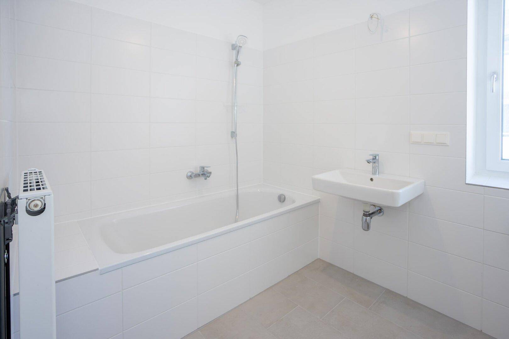Sauberes Badezimmer mit Badewanne, Waschbecken und weiß gefliesten Wänden.