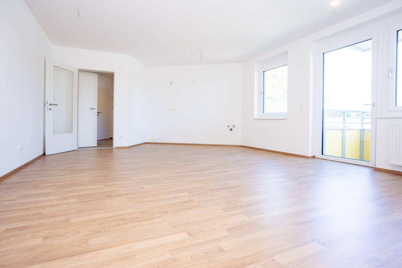 Geräumiges, helles Wohnzimmer mit Laminatboden und zwei Fenstern, bereit zur Einrichtung.