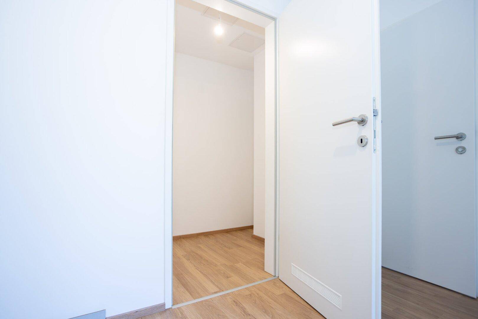 Heller Flur mit Laminatboden und weißer Tür, die in einen weiteren Raum führt.