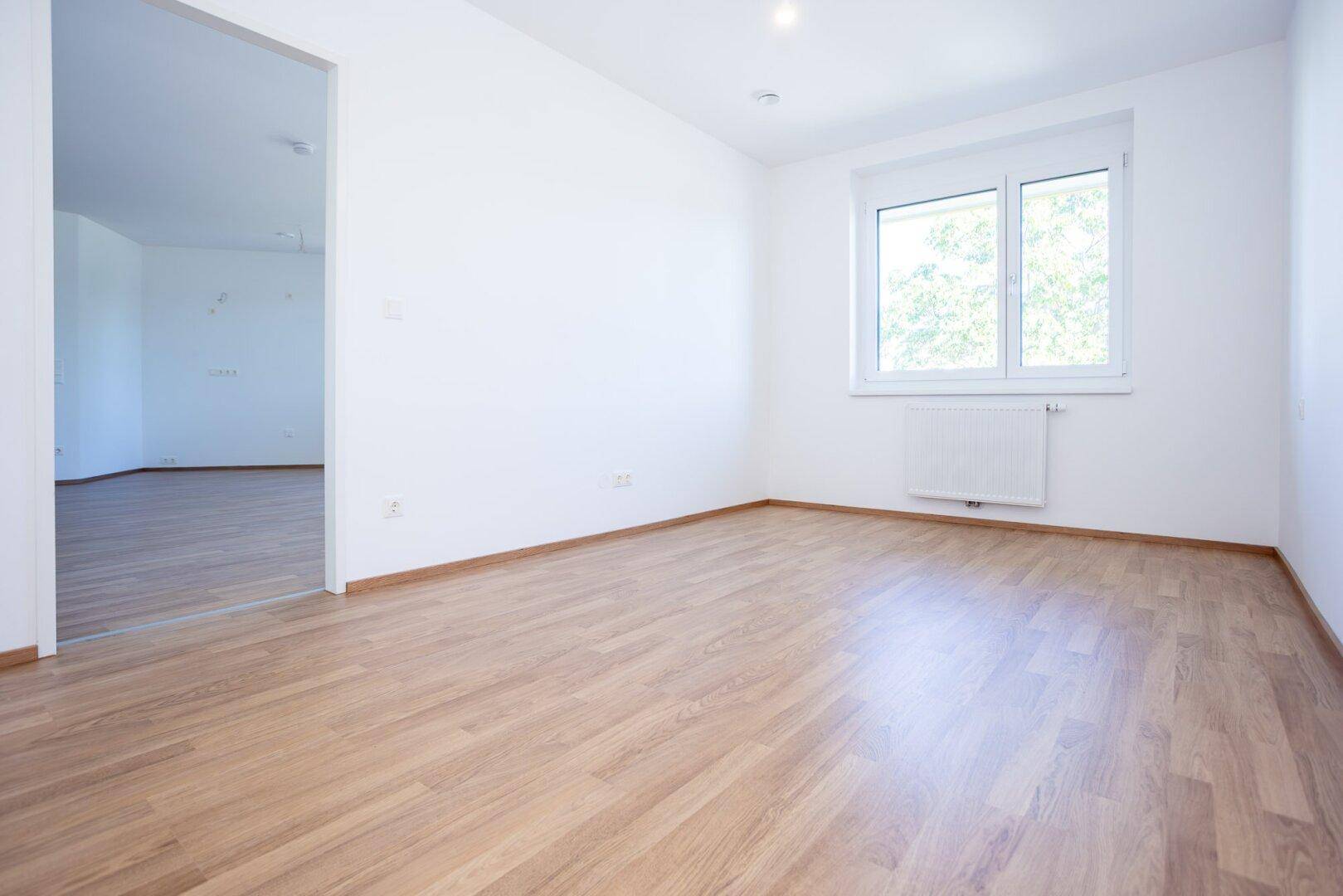 Helles Zimmer mit Laminatboden und großem Fenster, ideal als Schlaf- oder Arbeitszimmer.