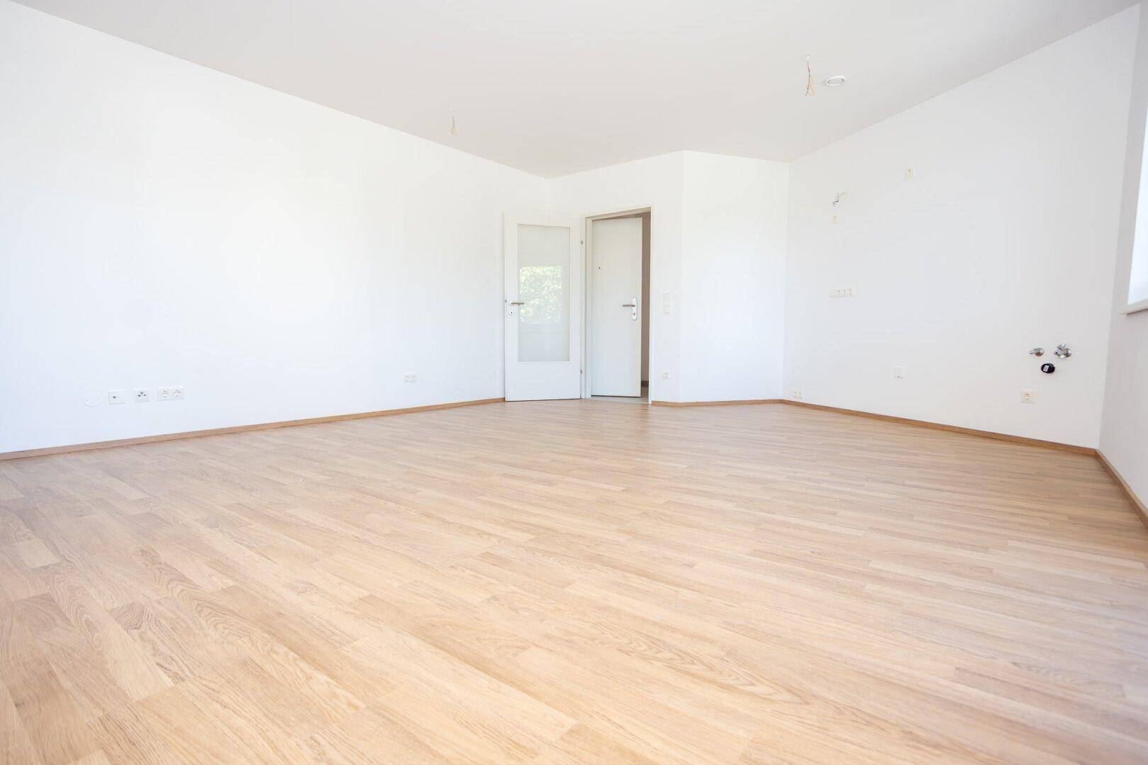 Leeres, helles Zimmer mit Laminatboden und einer Tür zu einem weiteren Raum.