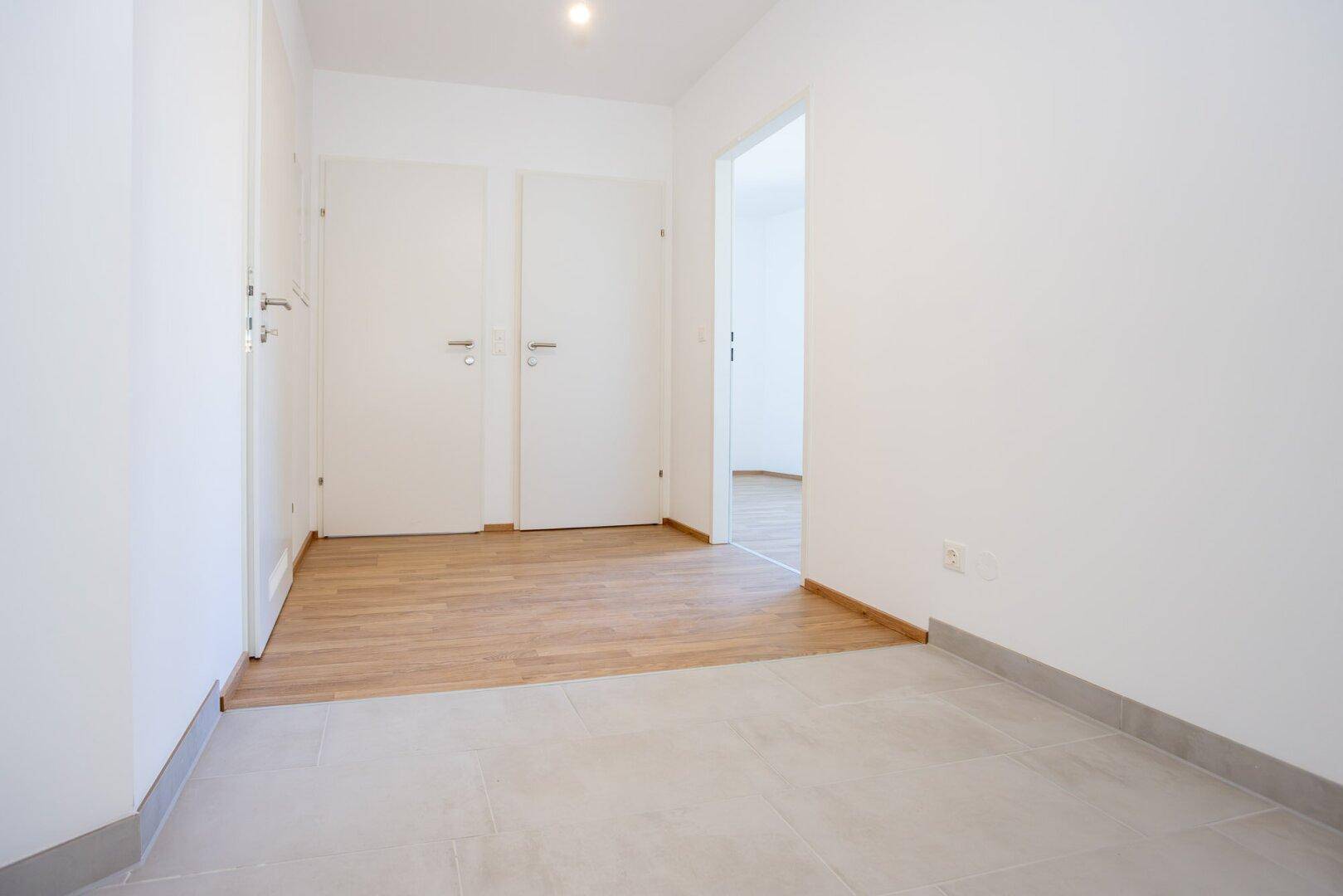 Eingangsbereich mit Fliesenboden, der in einen Raum mit Laminat übergeht.
