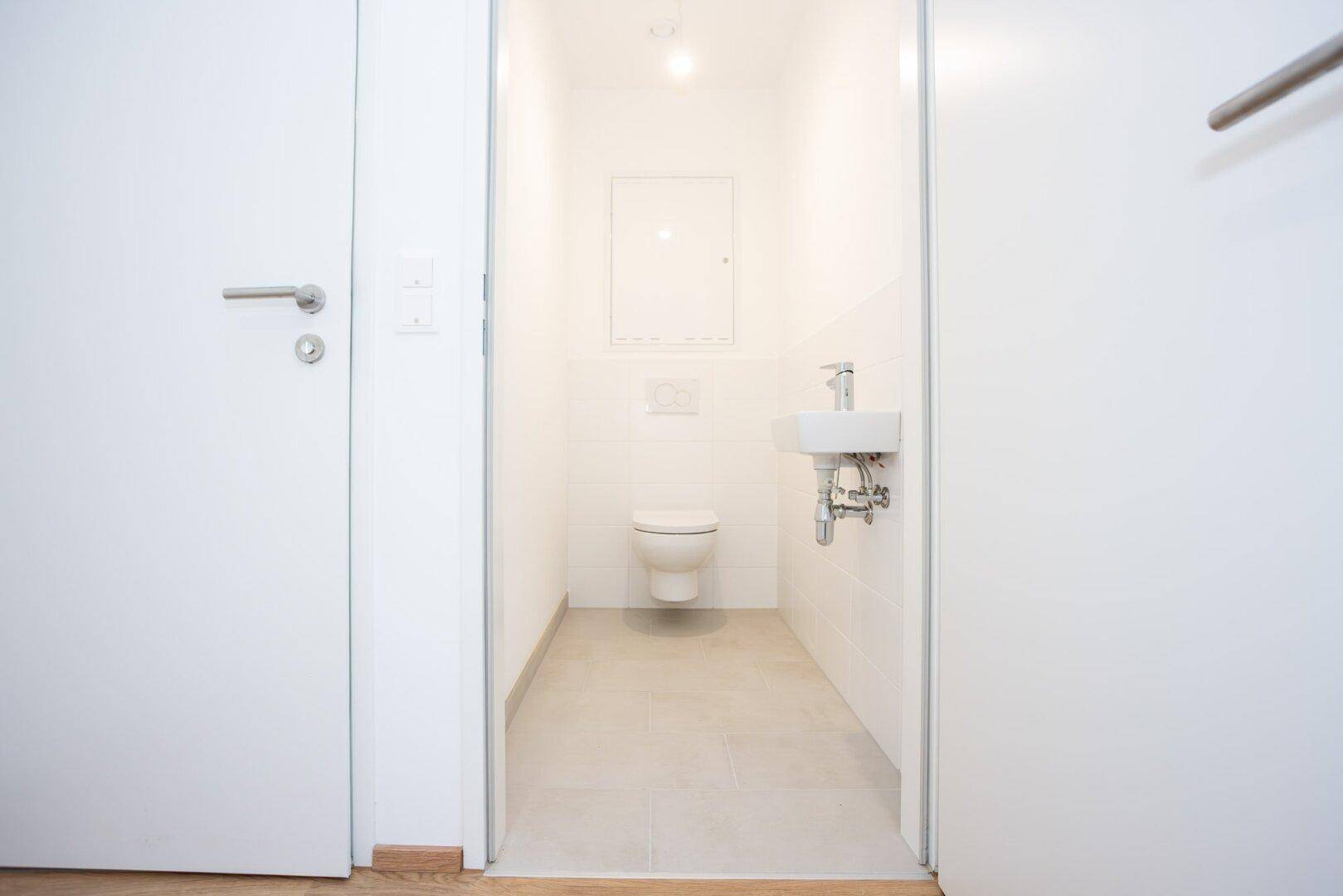 Separates Gäste-WC mit wandhängender Toilette und kleinem Handwaschbecken.