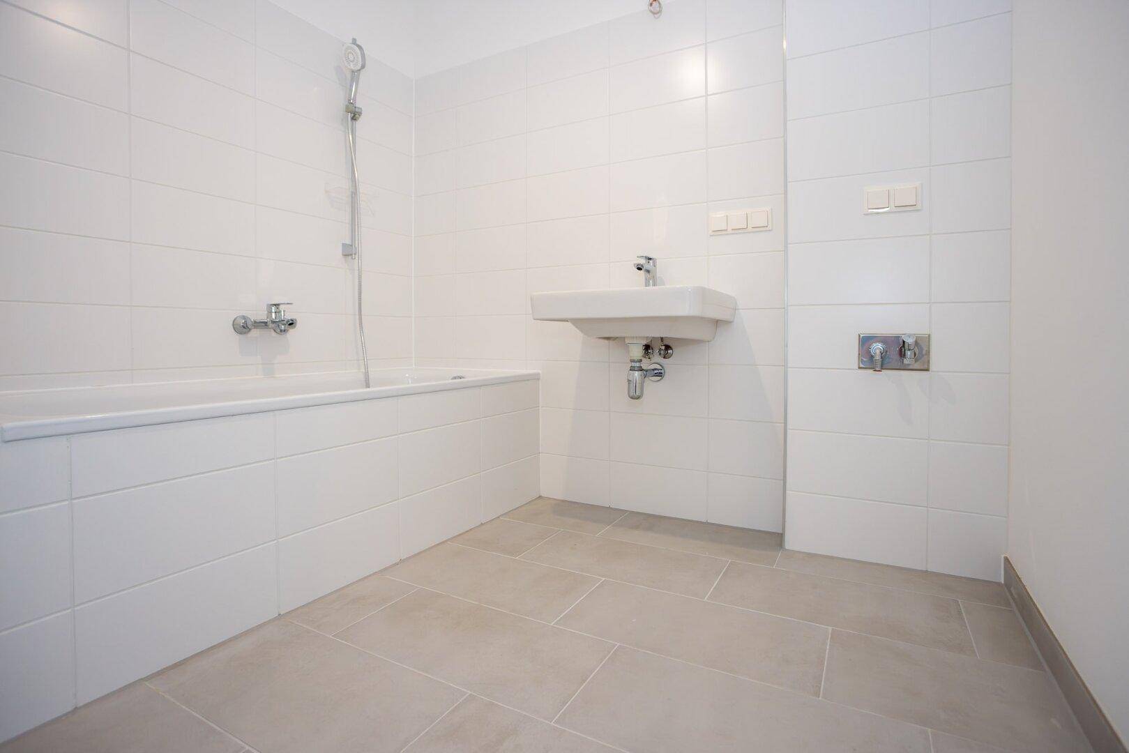 Modernes Badezimmer mit weißen Fliesen, Badewanne und Waschbecken.