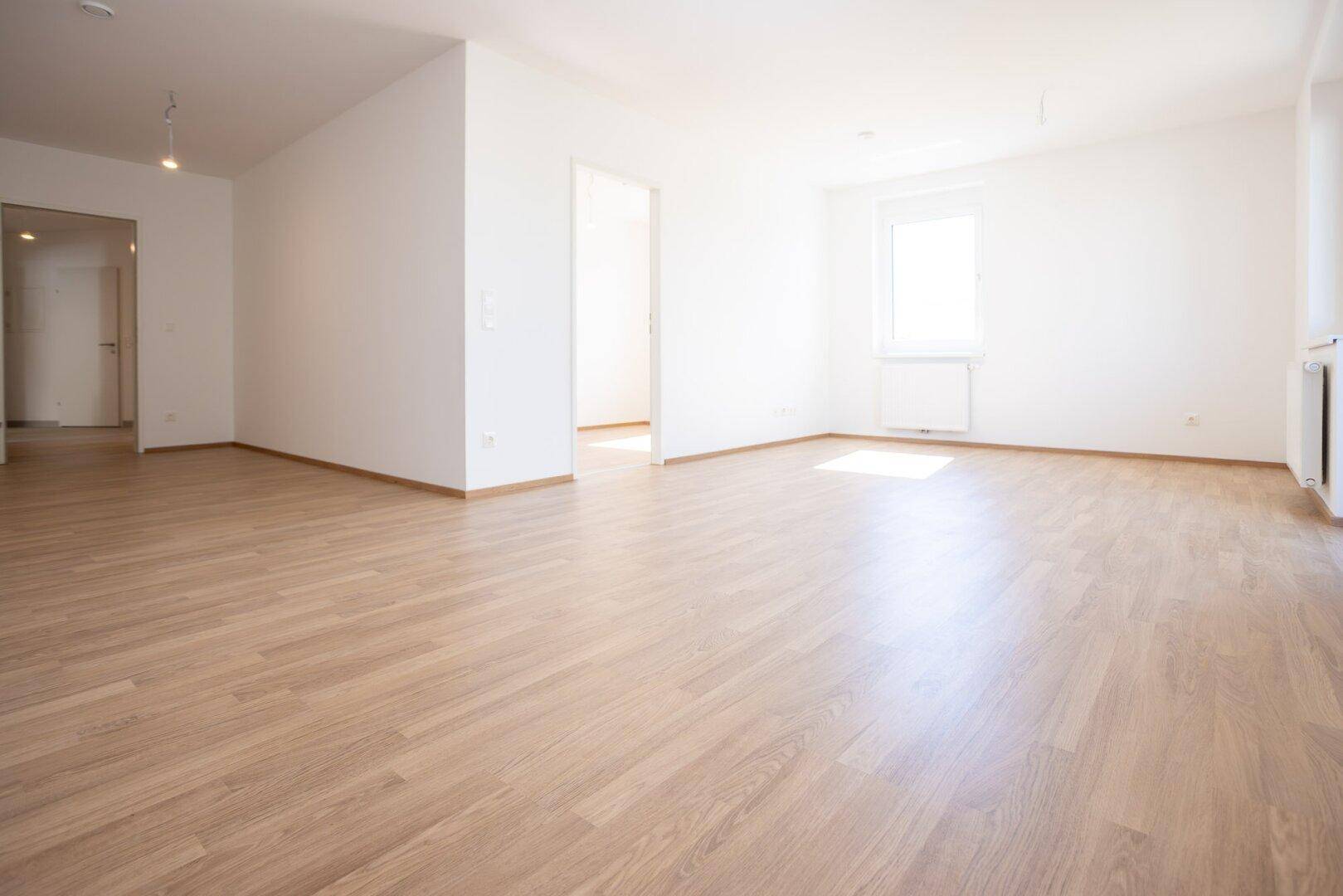 Geräumiges, helles Zimmer mit Laminatboden und mehreren Türöffnungen.