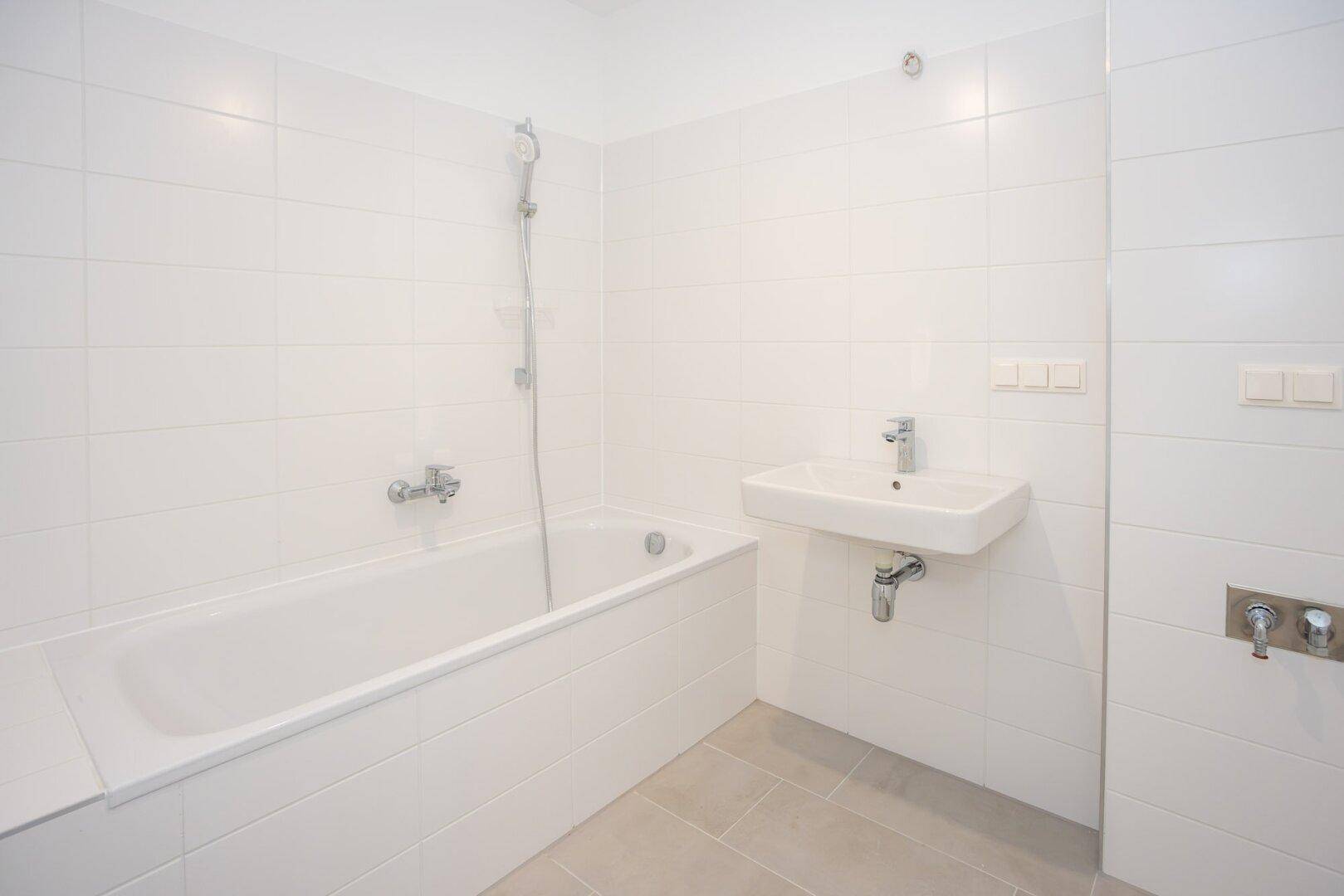 Helles Badezimmer mit Badewanne, Waschbecken und weißen Wandfliesen.